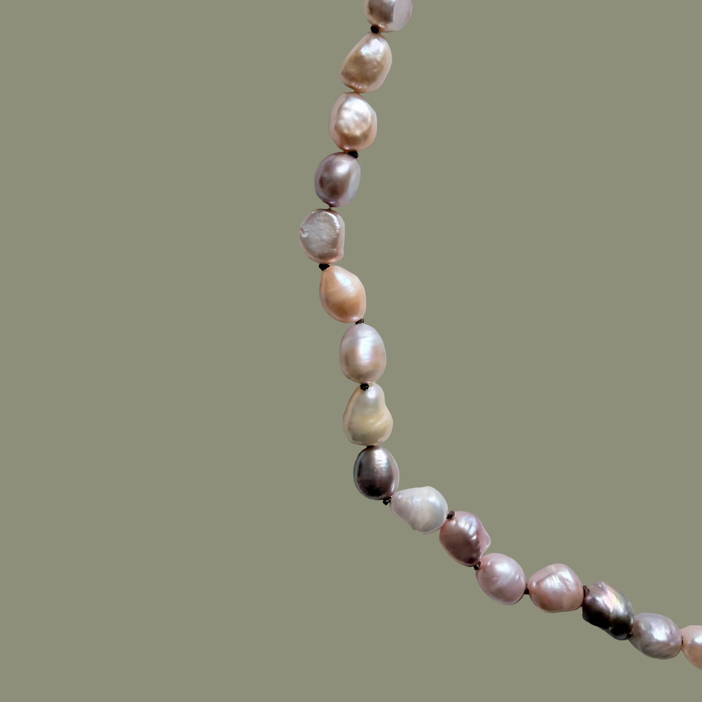 A strand of irregular baroque pearls in soft pink, cream, and lavender tones, laid out diagonally on a light gray background.