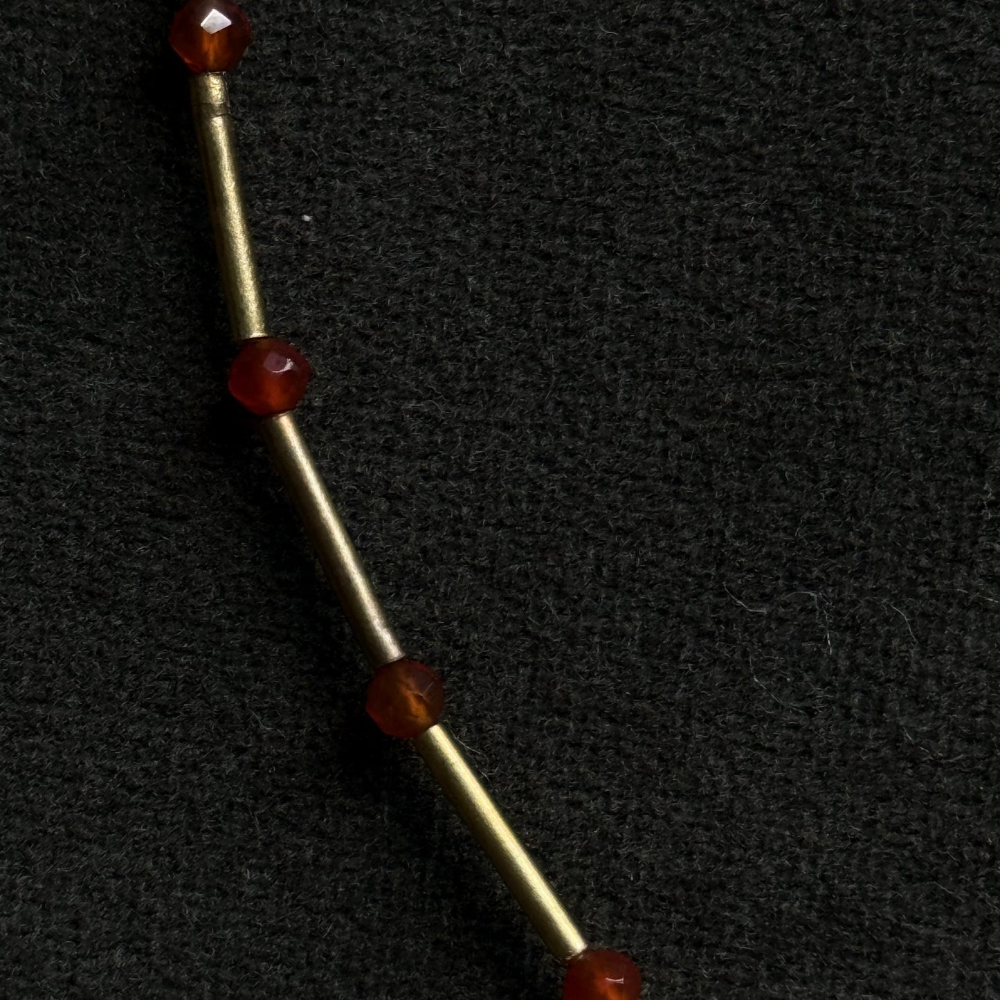 A close-up of a gold-toned metal chain or rod with four faceted dark red gemstone beads spaced along it, set against a textured black background.