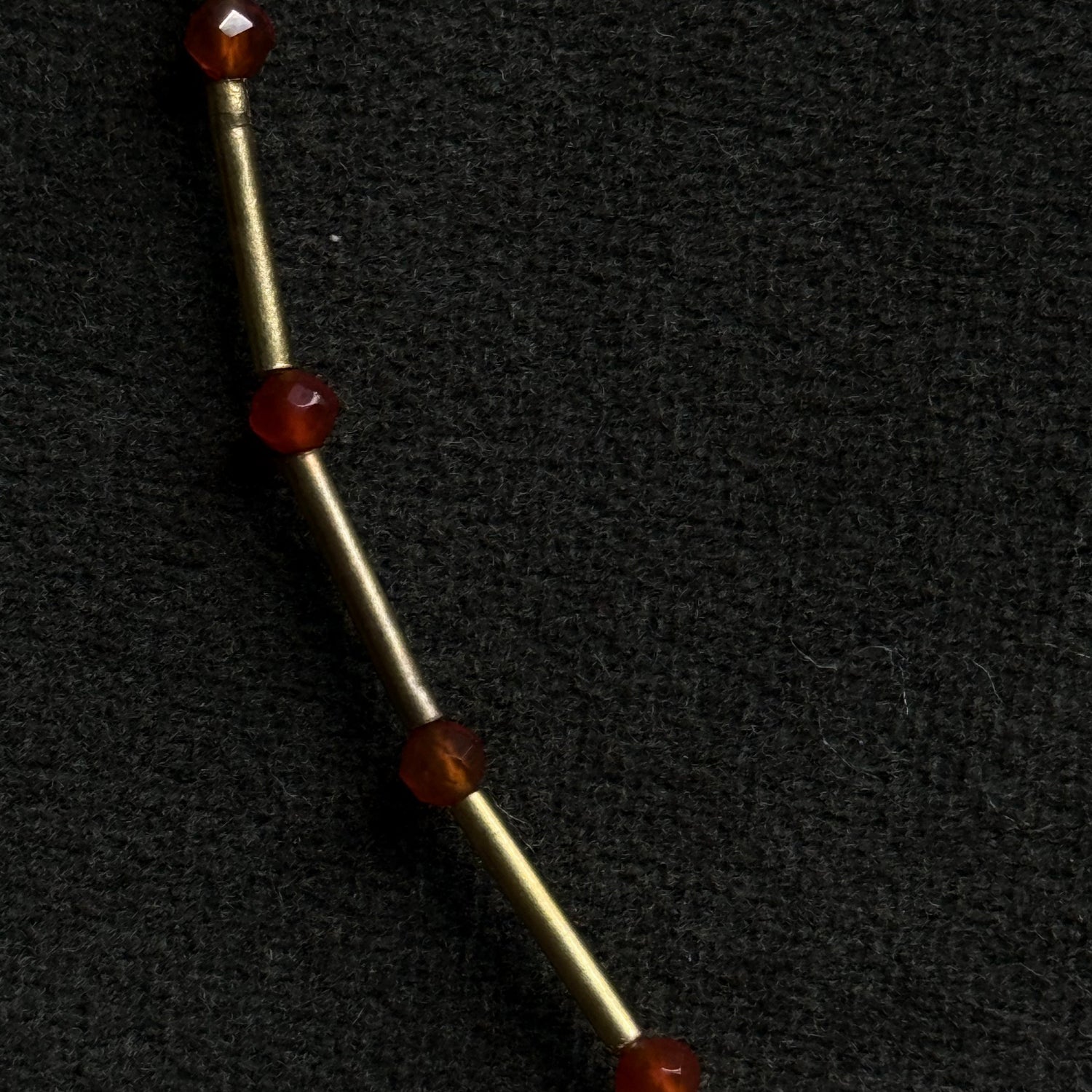 A close-up of a gold-toned metal chain or rod with four faceted dark red gemstone beads spaced along it, set against a textured black background.