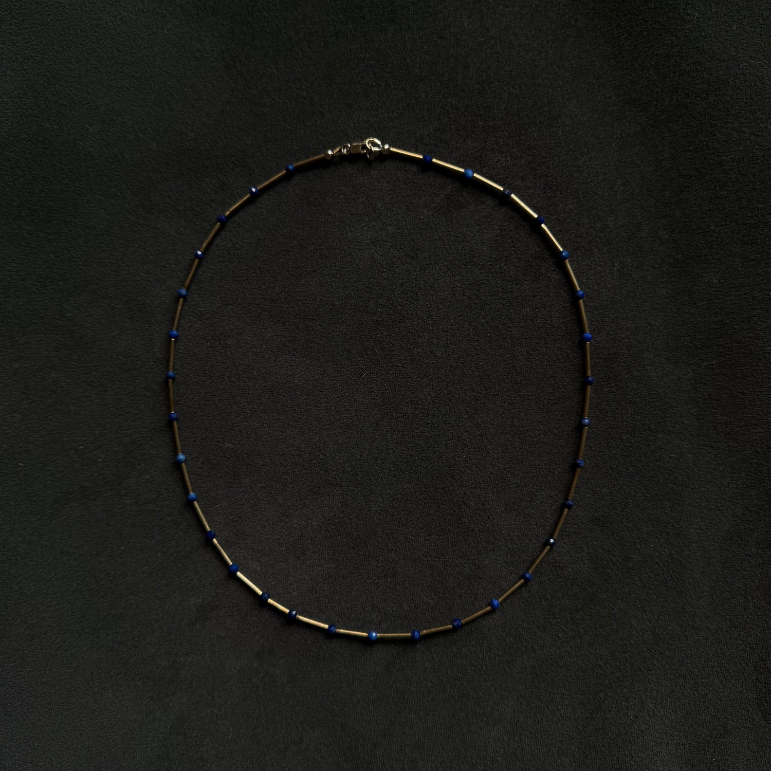 A delicate beaded necklace with alternating small gold and dark blue beads, arranged in a circle on a dark textured background.