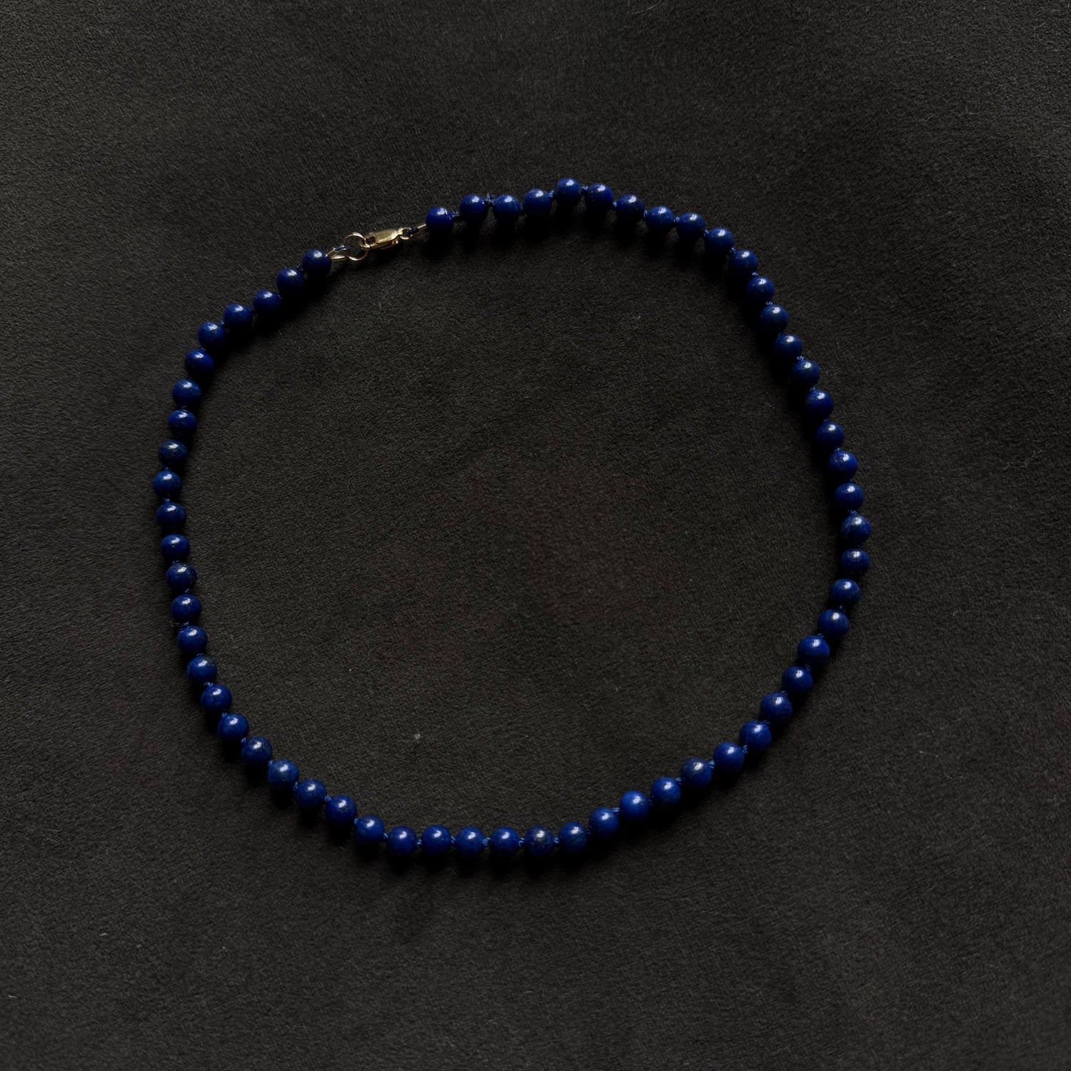 A beaded necklace made of small dark blue beads with a gold clasp, arranged in a circle on a dark textured background.