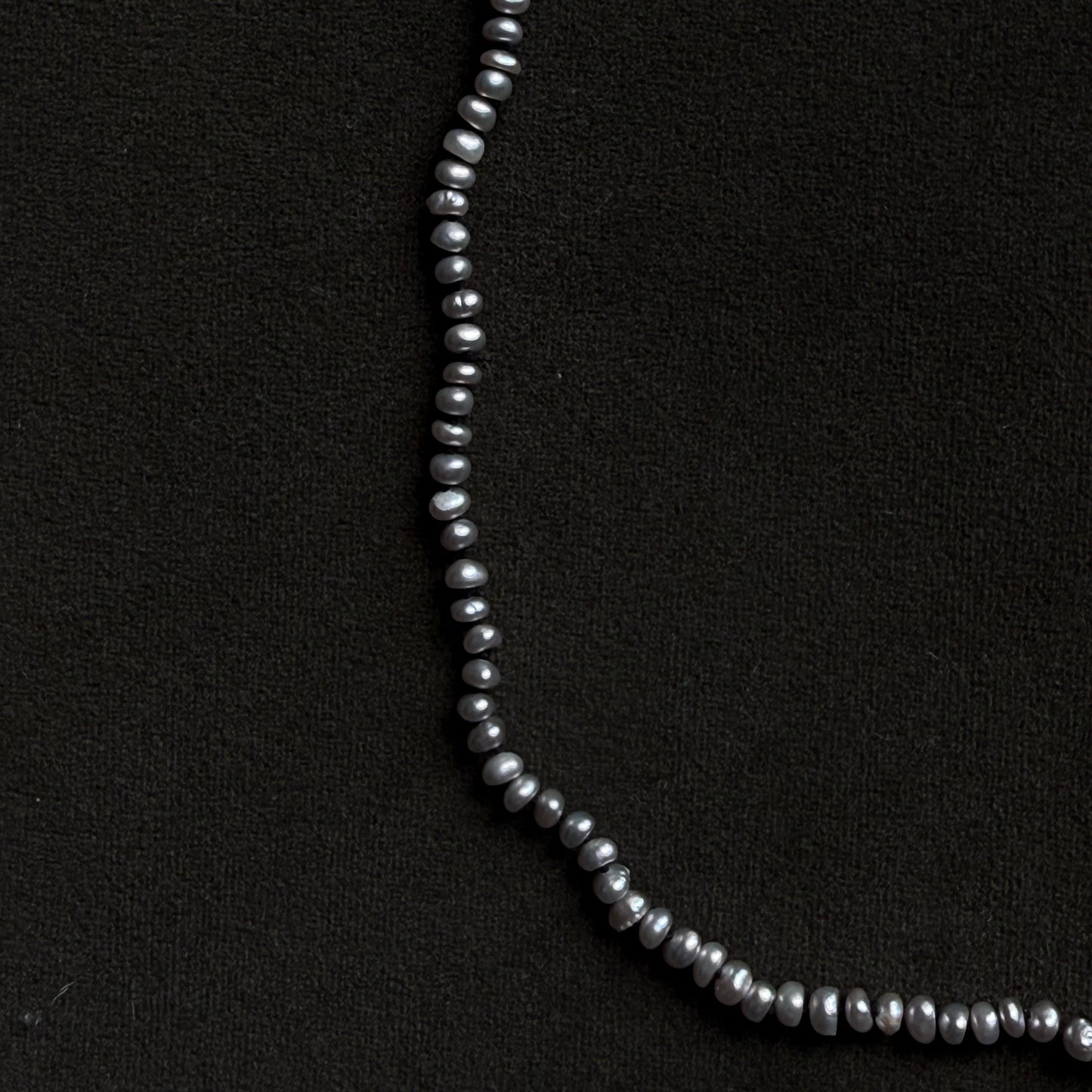 A strand of dark gray baroque pearls arranged in a curved line on a textured black background.