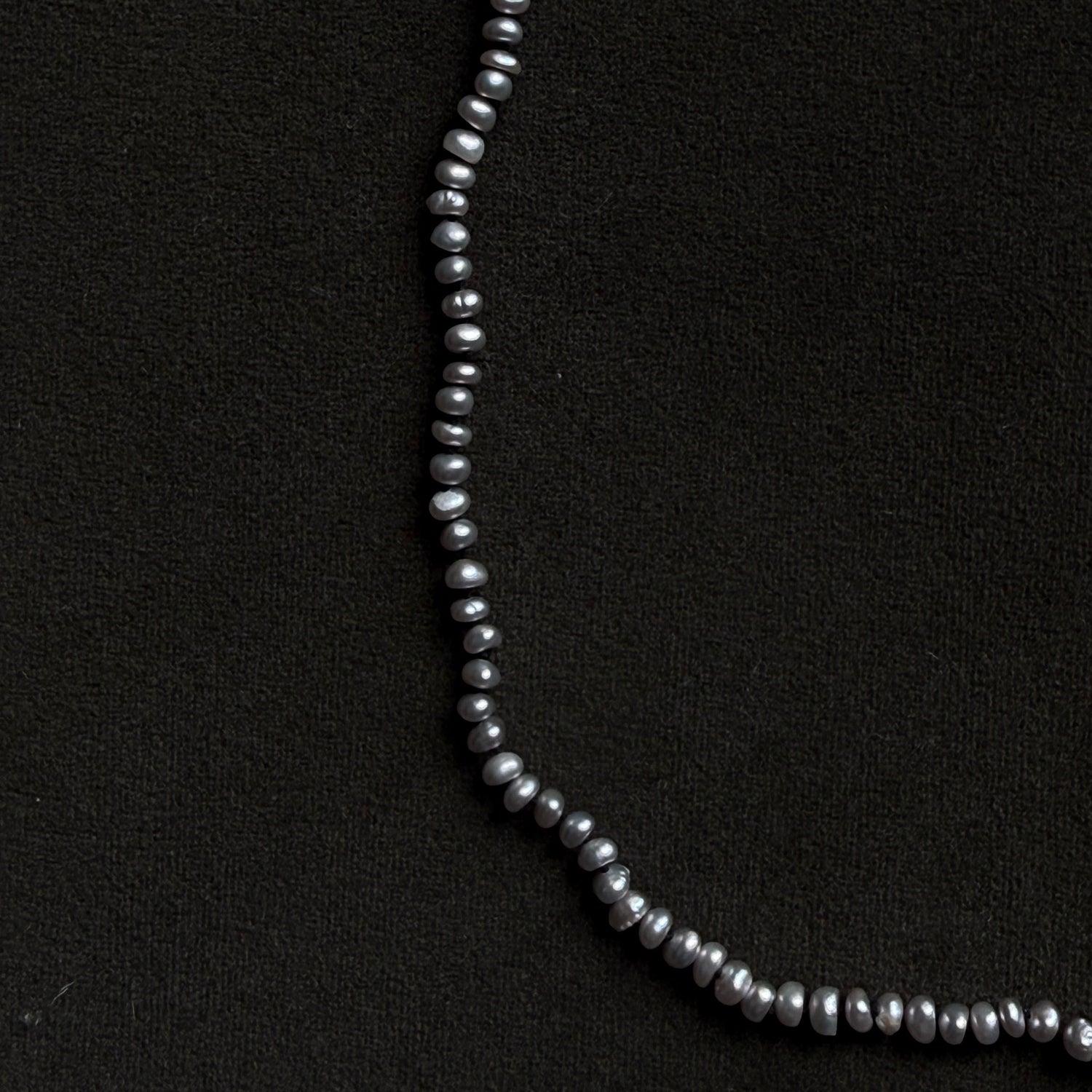 A strand of dark gray baroque pearls arranged in a curved line on a textured black background.