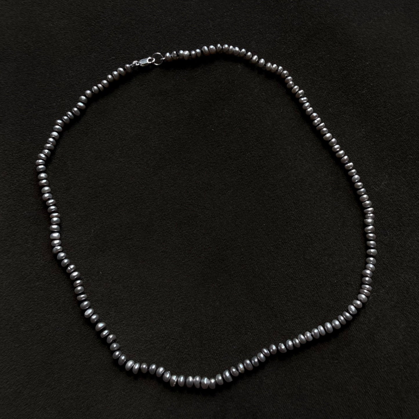 A dark gray freshwater pearl necklace arranged in a circle on a black textured background.