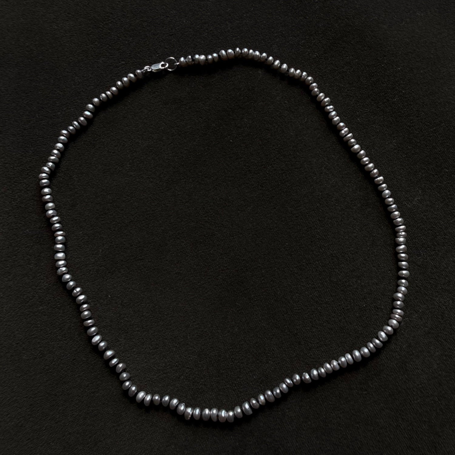 A dark gray freshwater pearl necklace arranged in a circle on a black textured background.