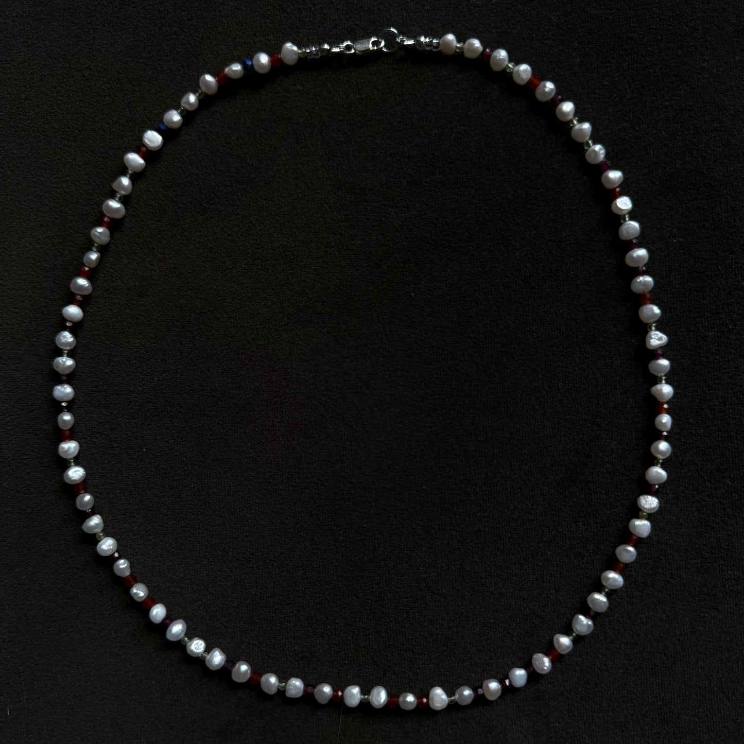 A beaded pearl necklace with small silver-toned spacer beads, arranged in a circle on a solid black background.