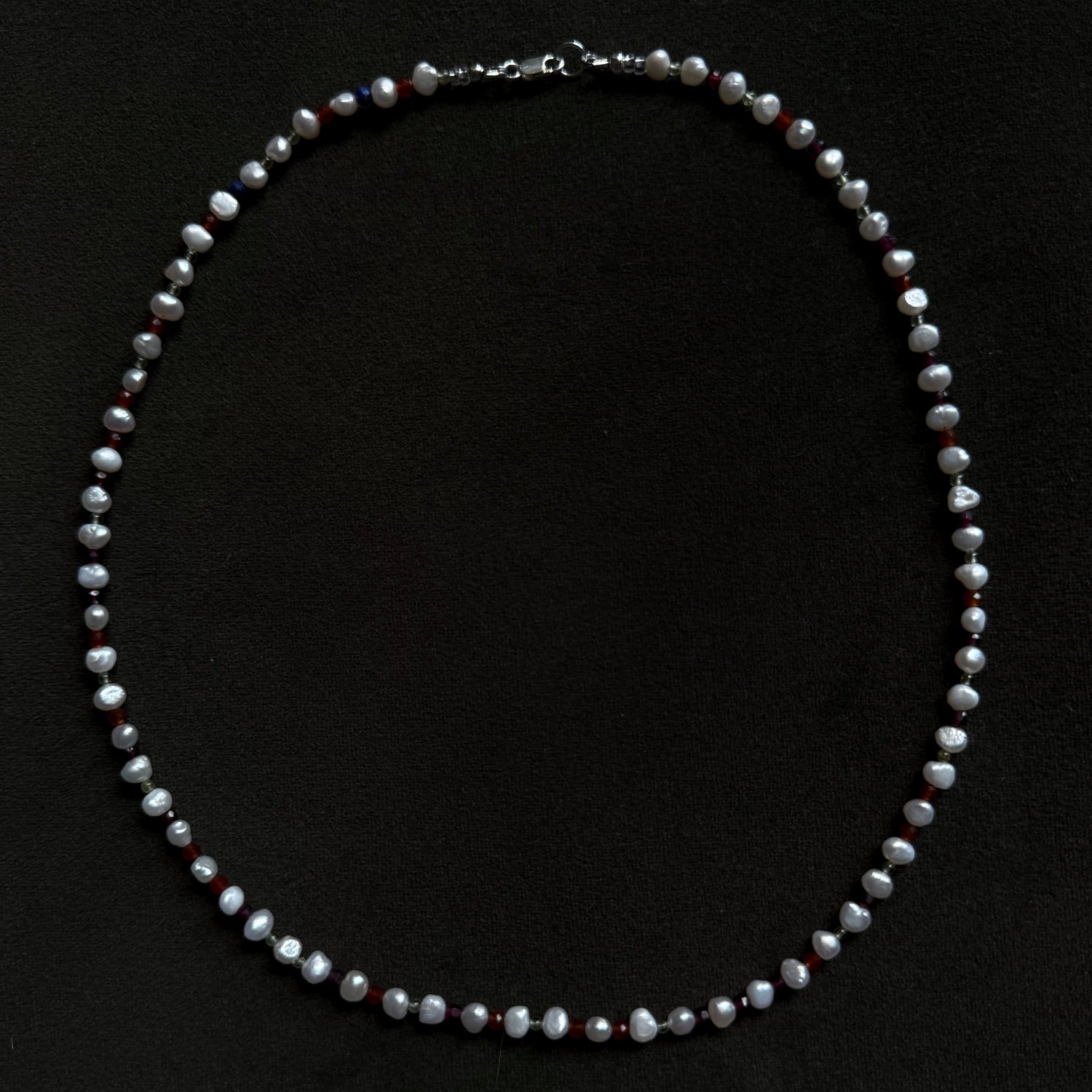 A beaded pearl necklace with small silver-toned spacer beads, arranged in a circle on a solid black background.