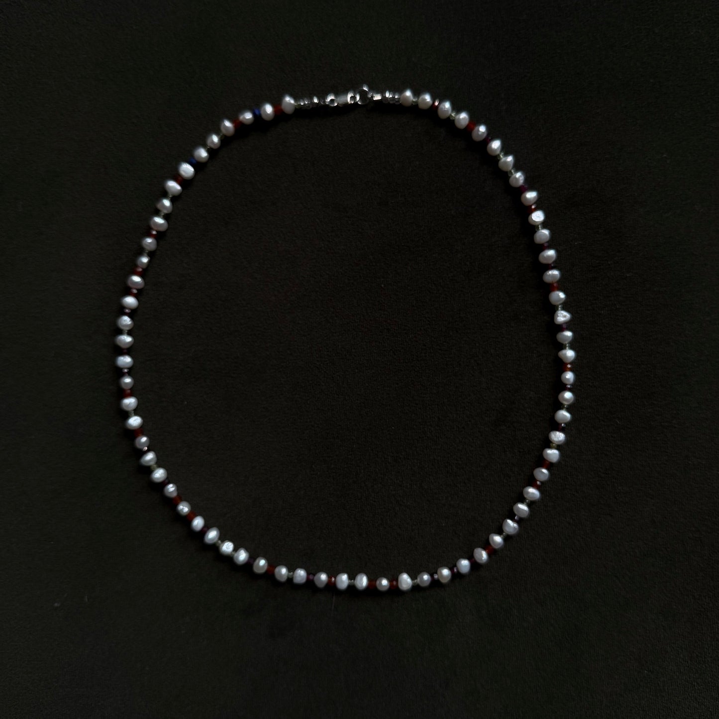 A single-strand pearl necklace with a silver clasp, laid flat on a solid black background.