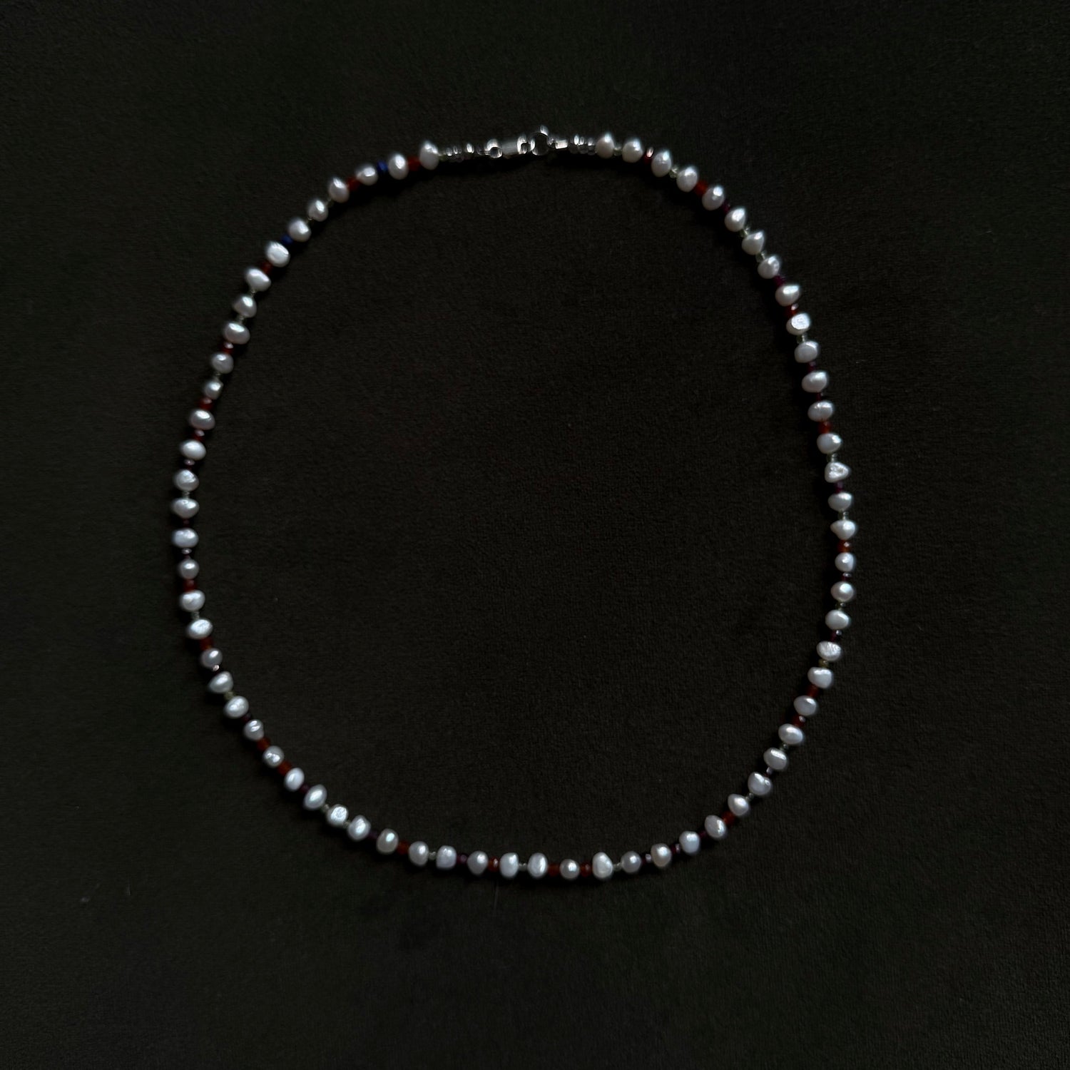 A single-strand pearl necklace with a silver clasp, laid flat on a solid black background.