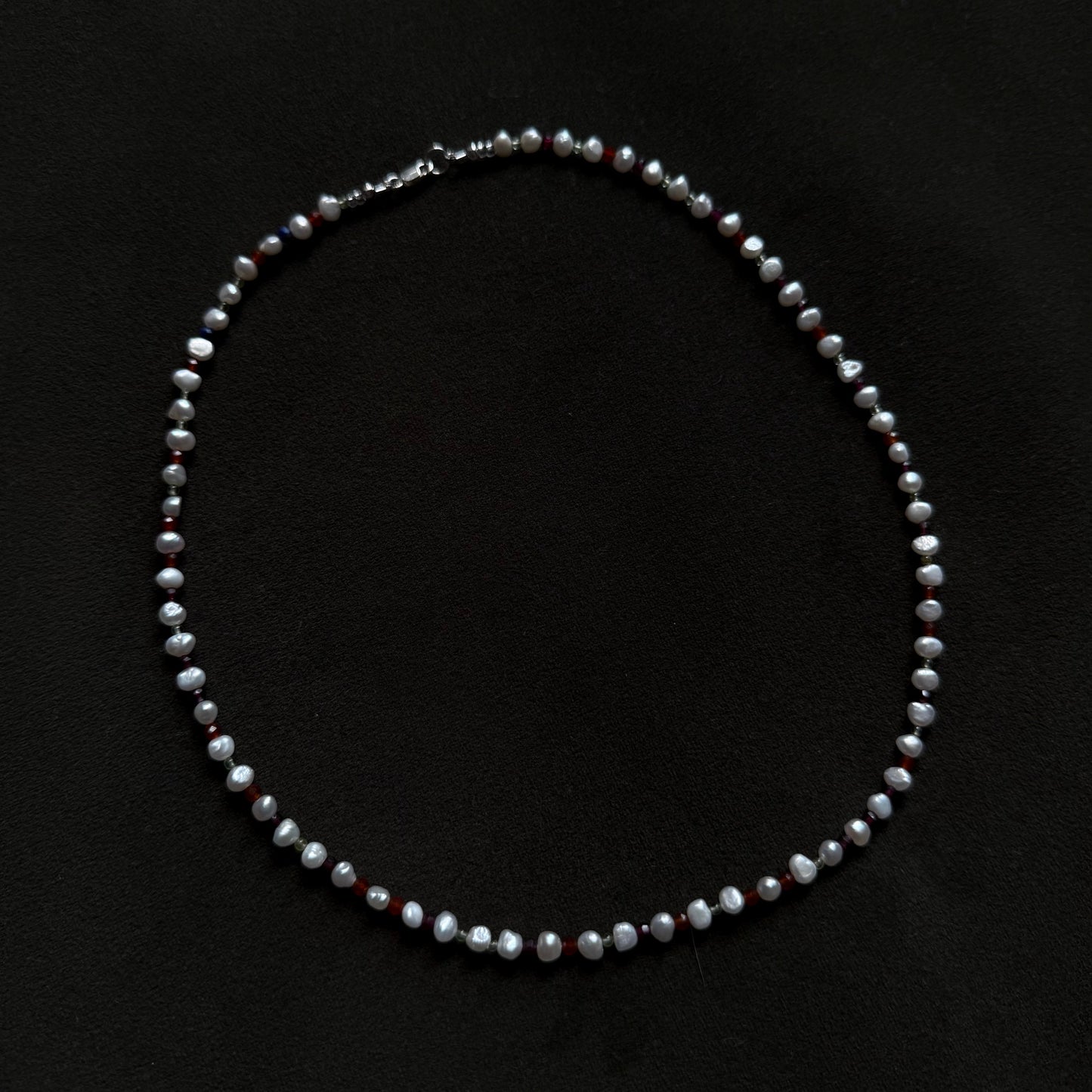 A beaded necklace made of small gray and white faceted beads with subtle dark red accents, displayed on a black background.