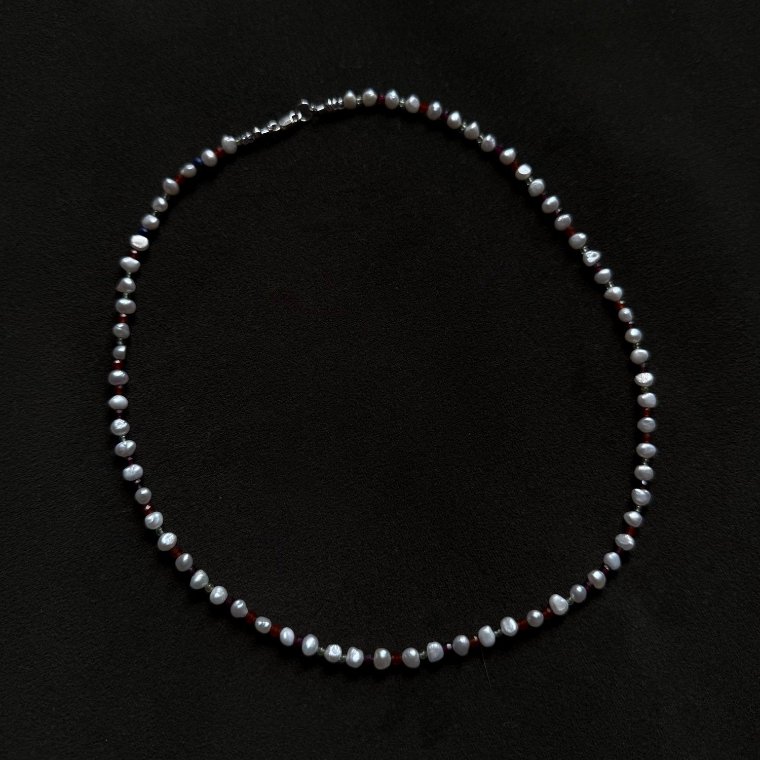 A beaded necklace made of small gray and white faceted beads with subtle dark red accents, displayed on a black background.