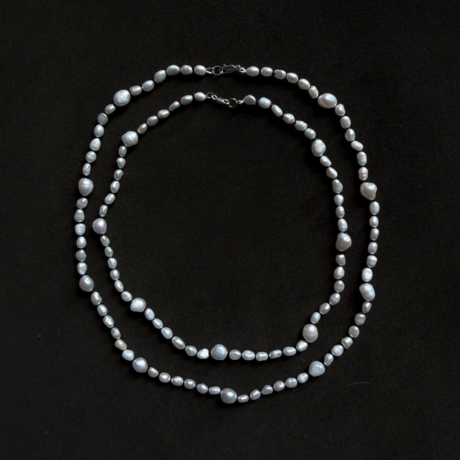 A double-strand pearl necklace with silver-toned metal findings, arranged in two overlapping loops on a solid black background.