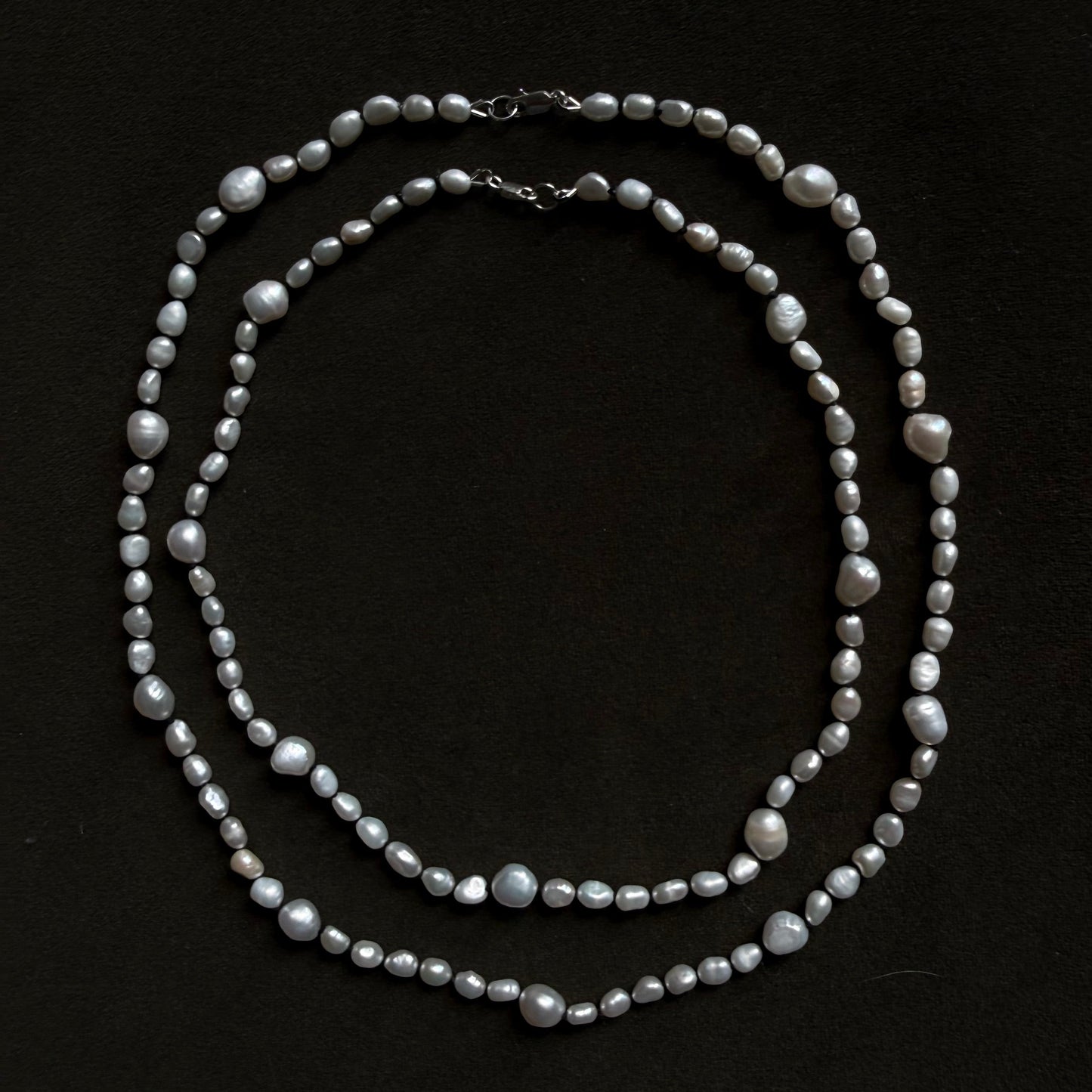 A double-strand baroque pearl necklace with silver-toned metal clasp, displayed on a solid black background.