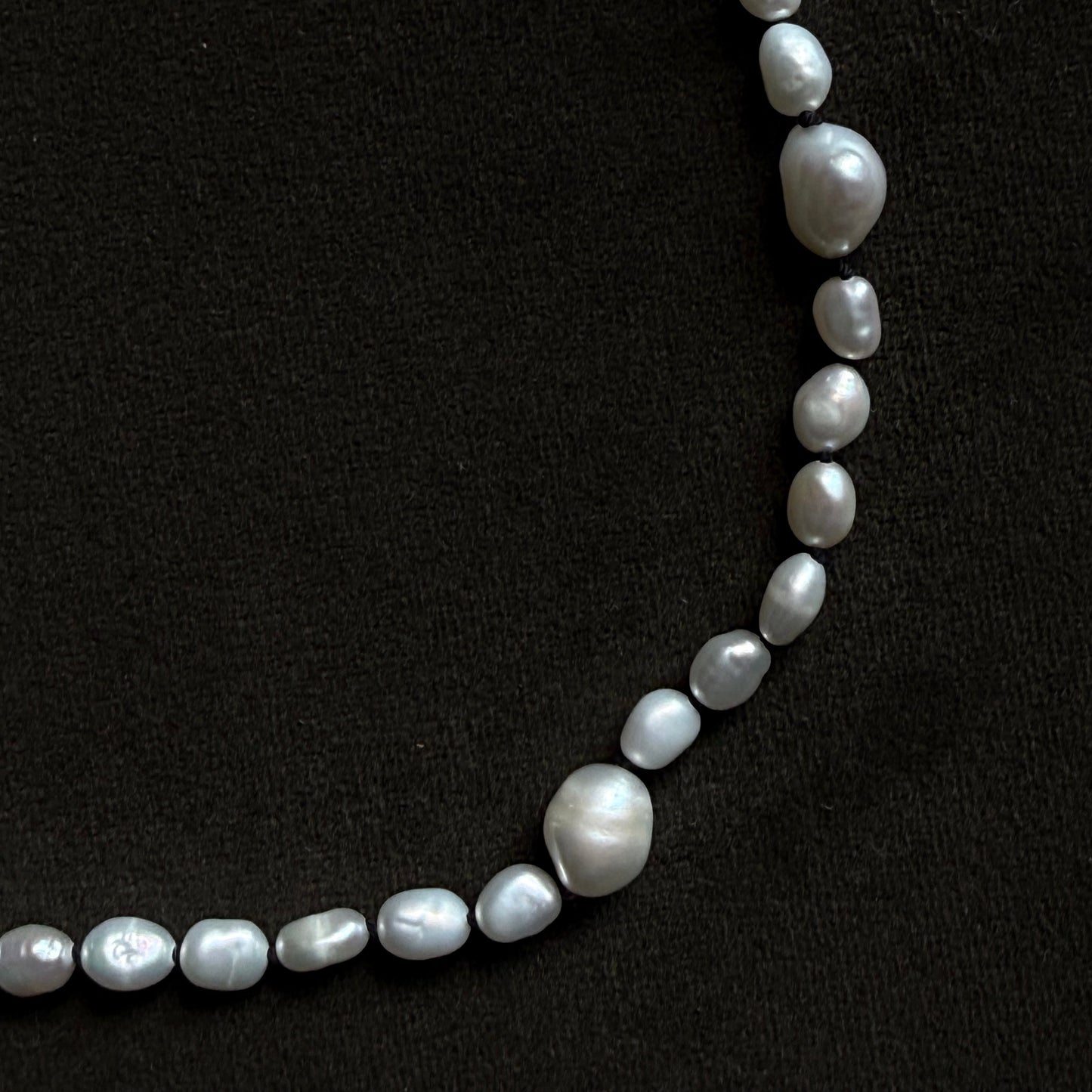 A strand of irregular baroque-style white pearls laid out in a curved line against a solid black background.