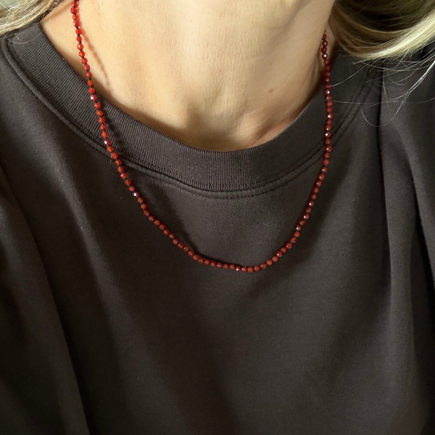 A close-up of a person wearing a dark charcoal gray sweatshirt and a red beaded necklace.