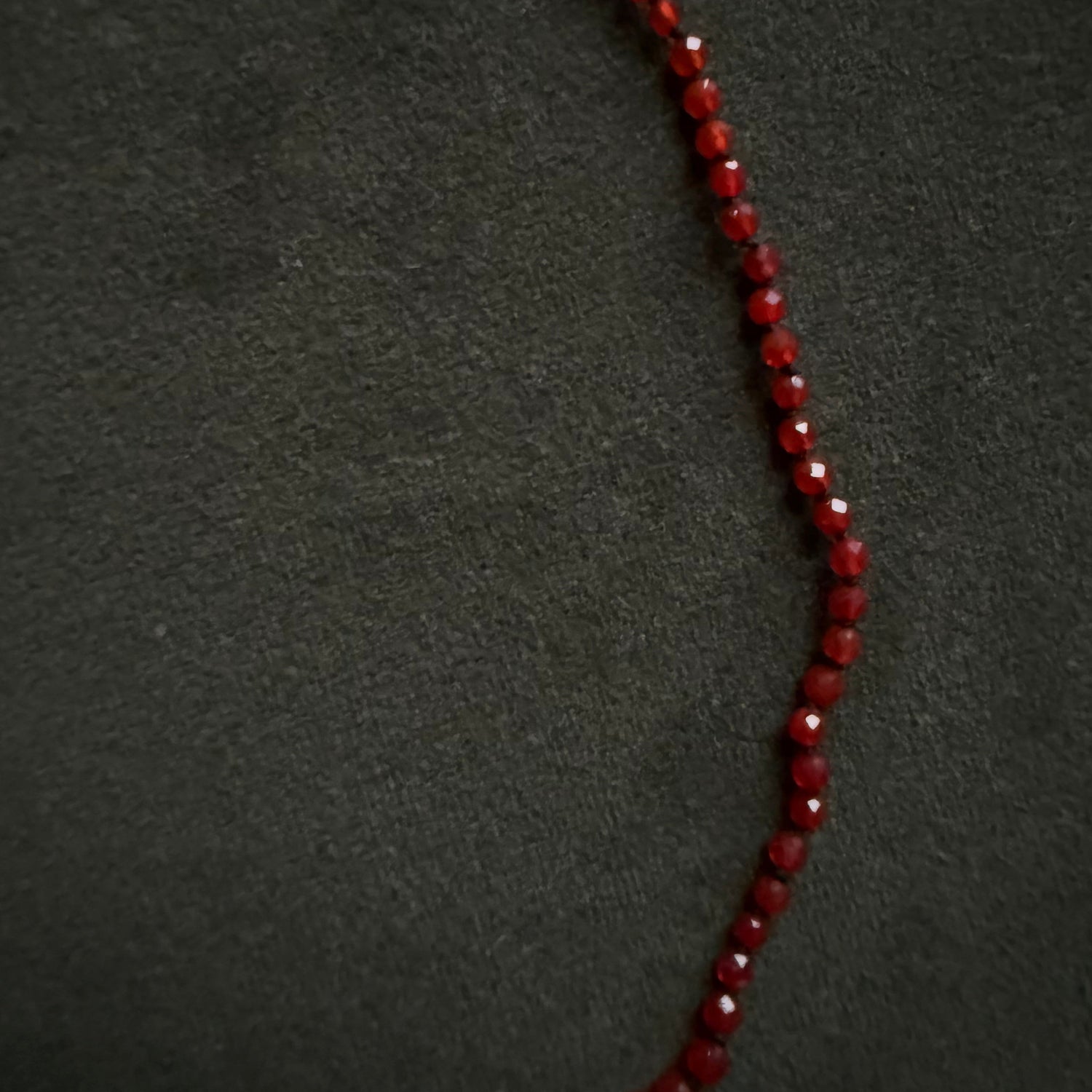 A strand of faceted deep red beads, likely garnet, arranged in a curved line on a dark textured background.