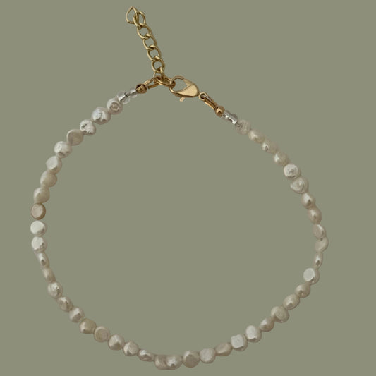 Pearl bracelet with gold chain on a light gray background
