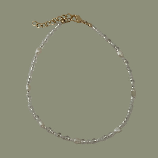 Bracelet with gold clasp and clear beads on a light gray background
