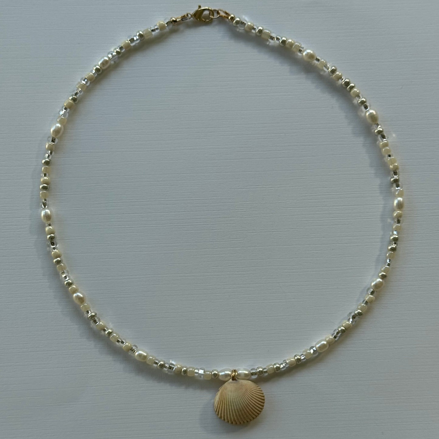 Gold anklet with a shell charm on a light gray background