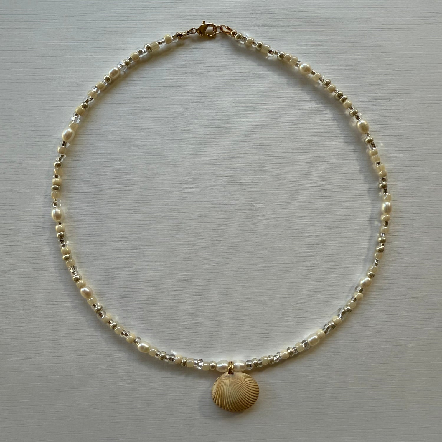Gold chain necklace with a shell pendant on a light gray background