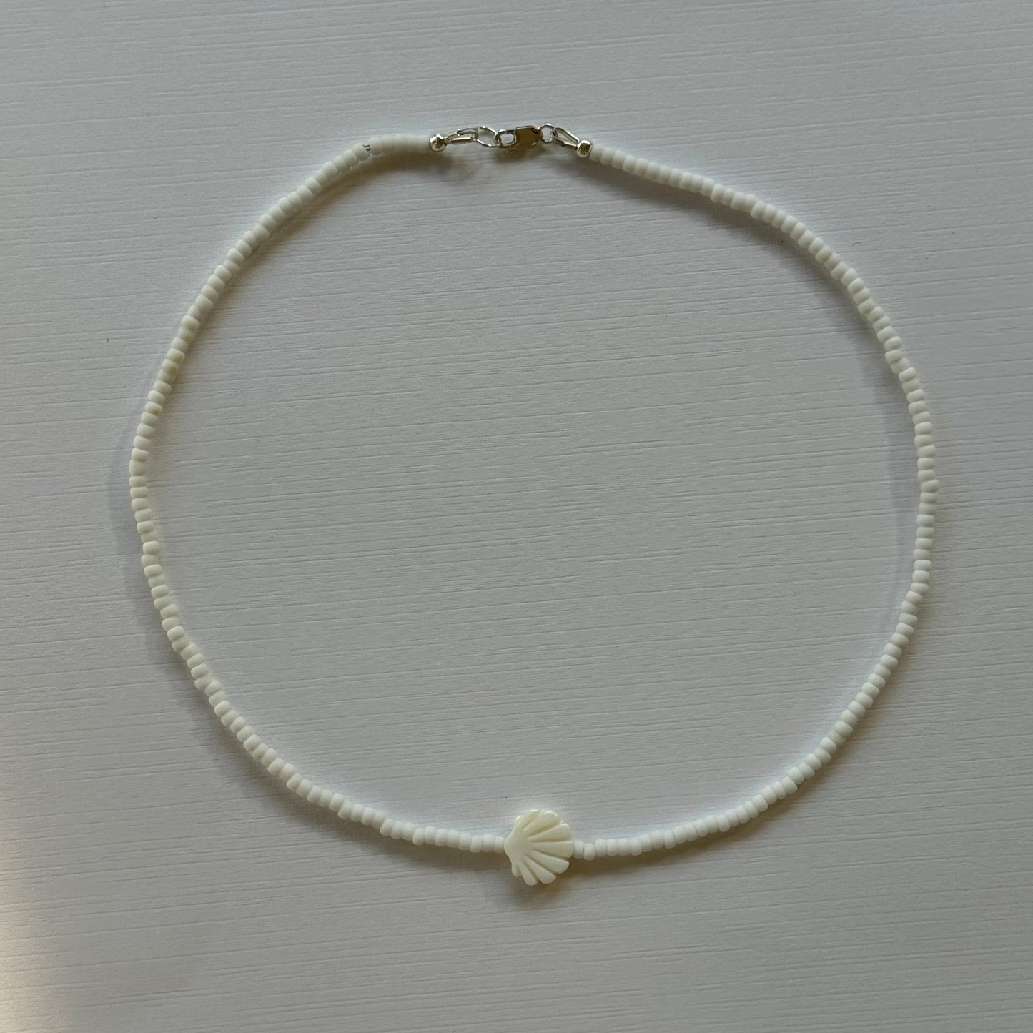 Pearl necklace with a shell charm on a light gray background