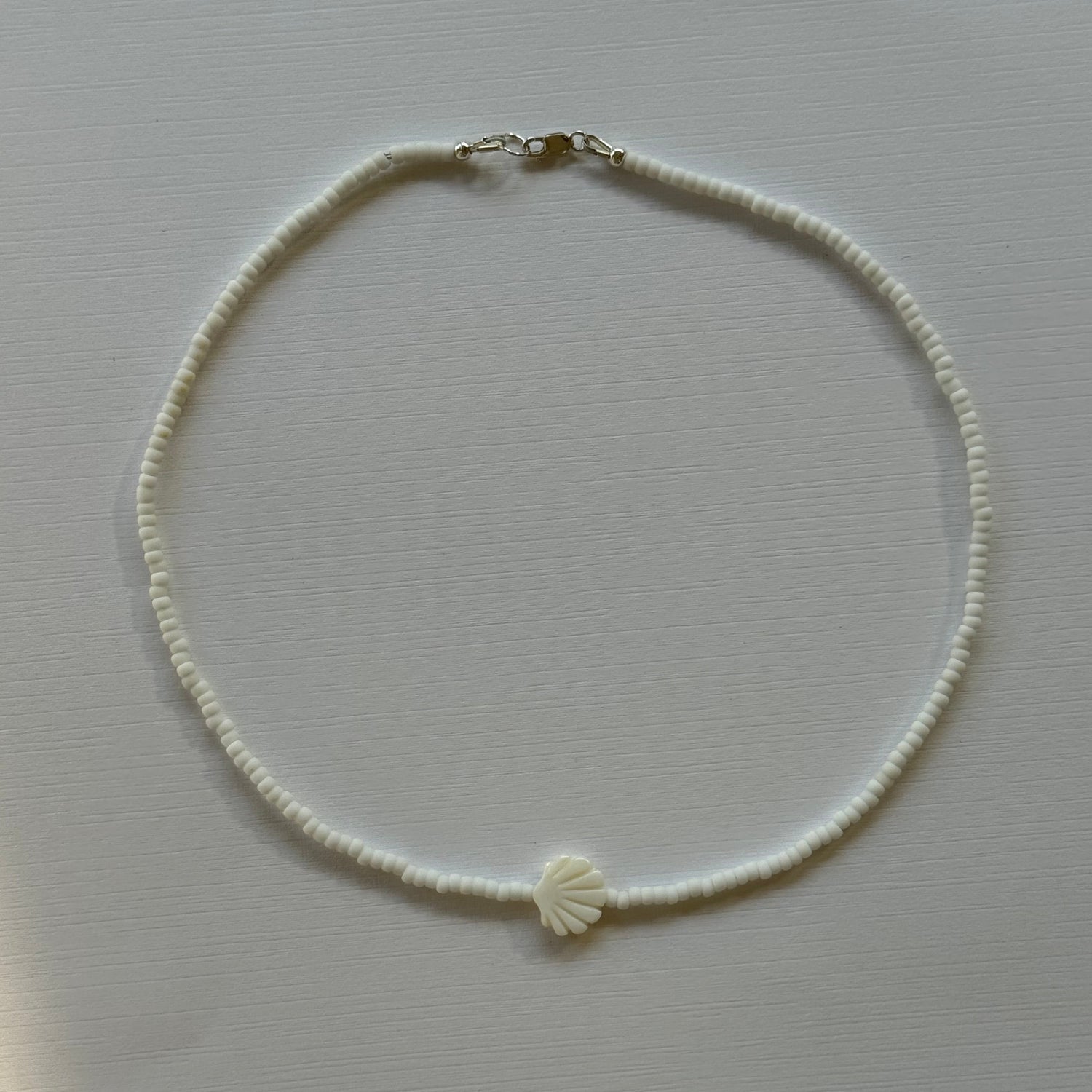 Pearl necklace with a shell charm on a light gray background