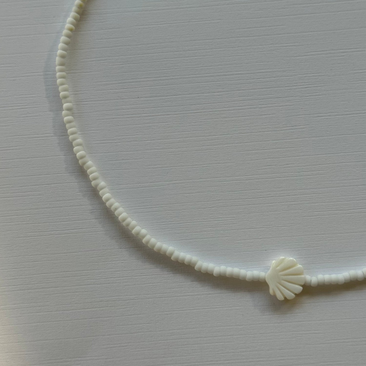 White cord with a shell charm on a light gray background