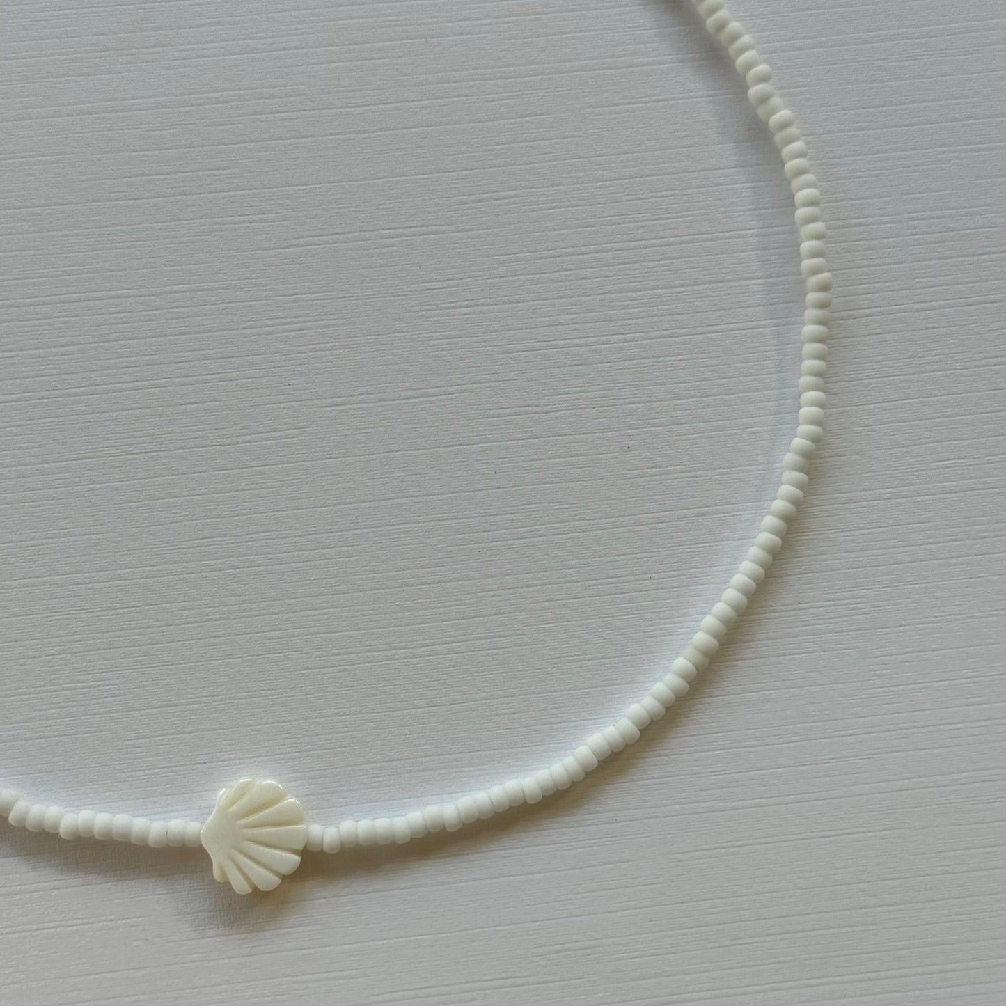 White shell charm on a thin white cord against a light gray background