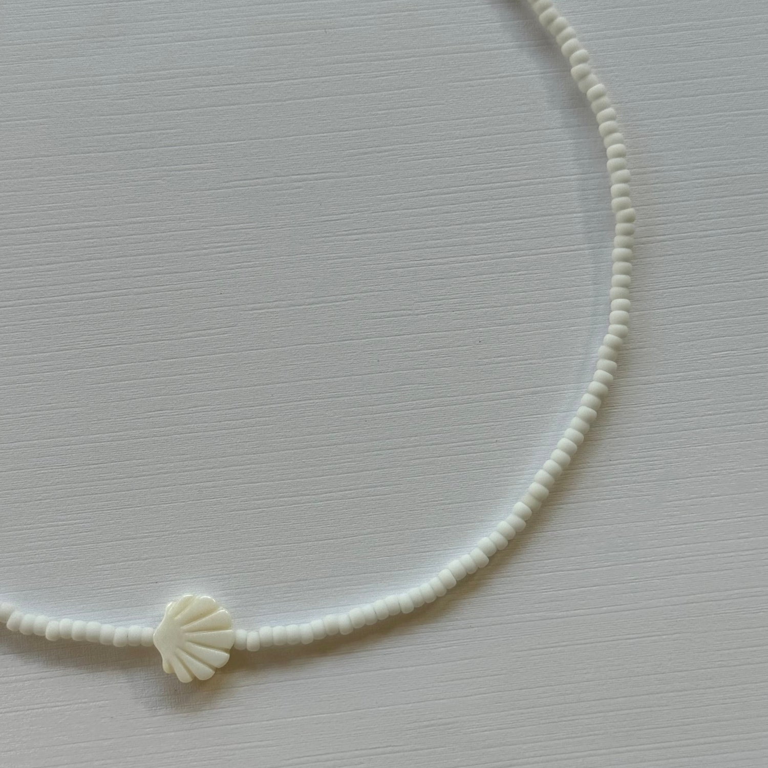 White shell charm on a thin white cord against a light gray background