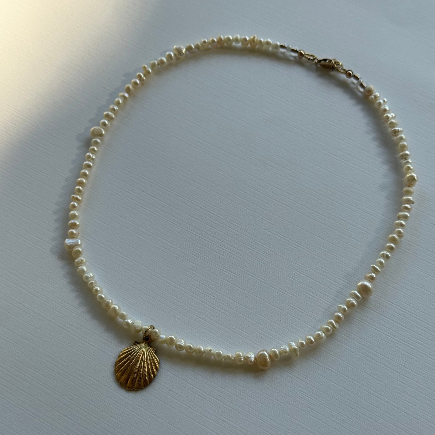 Pearl necklace with a shell pendant on a light gray background