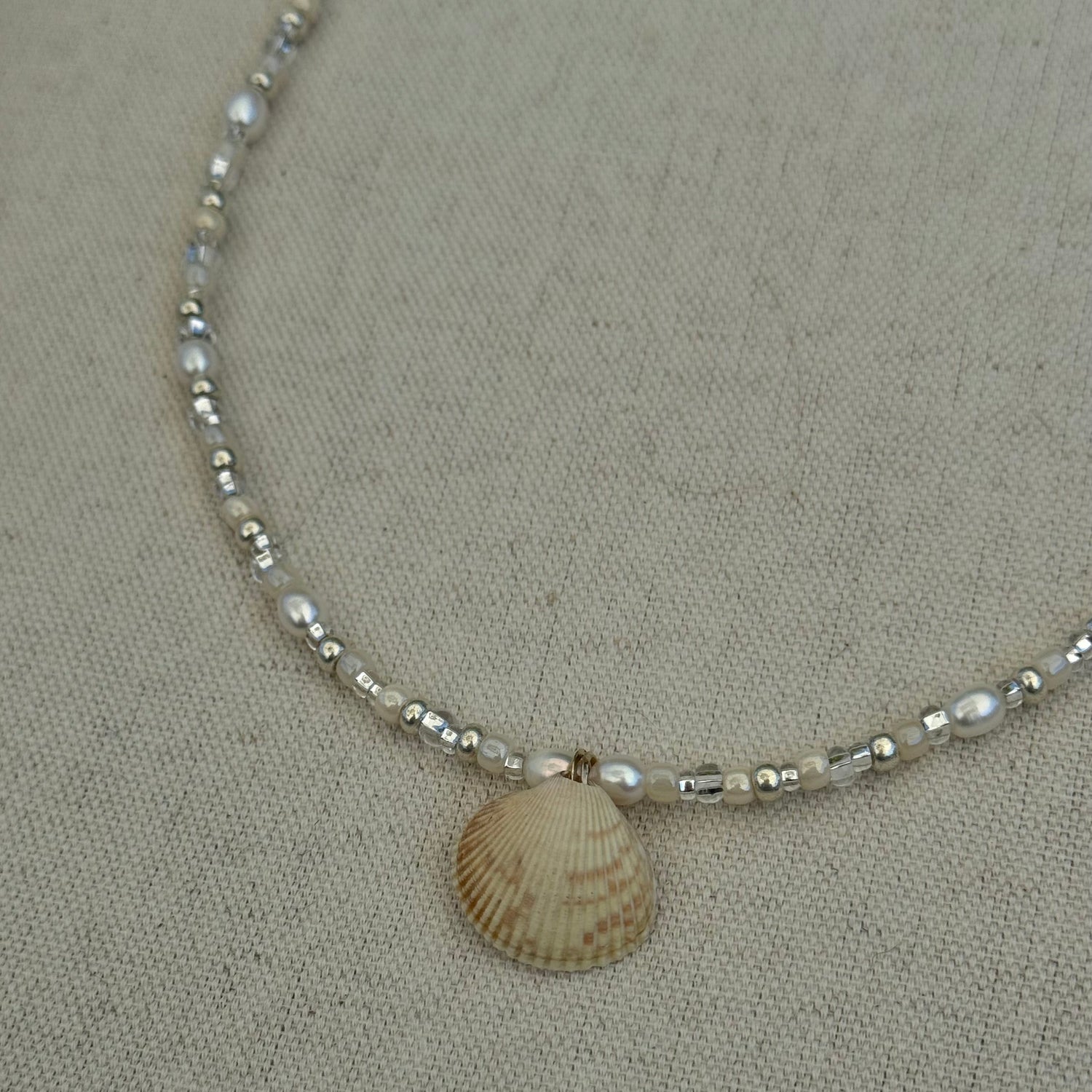Necklace with shell pendant on a beige fabric background