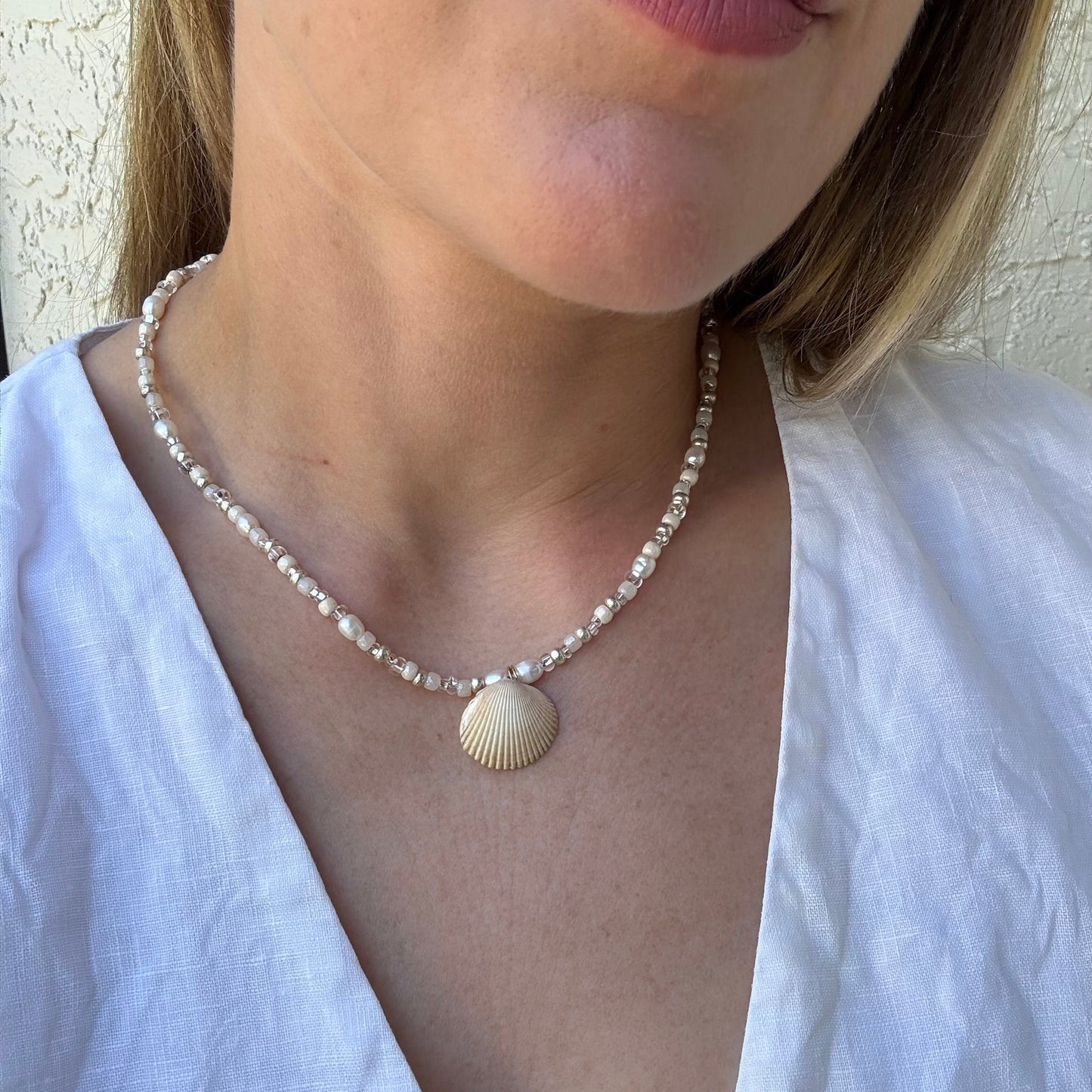 Person wearing a pearl necklace with a shell pendant against a neutral background