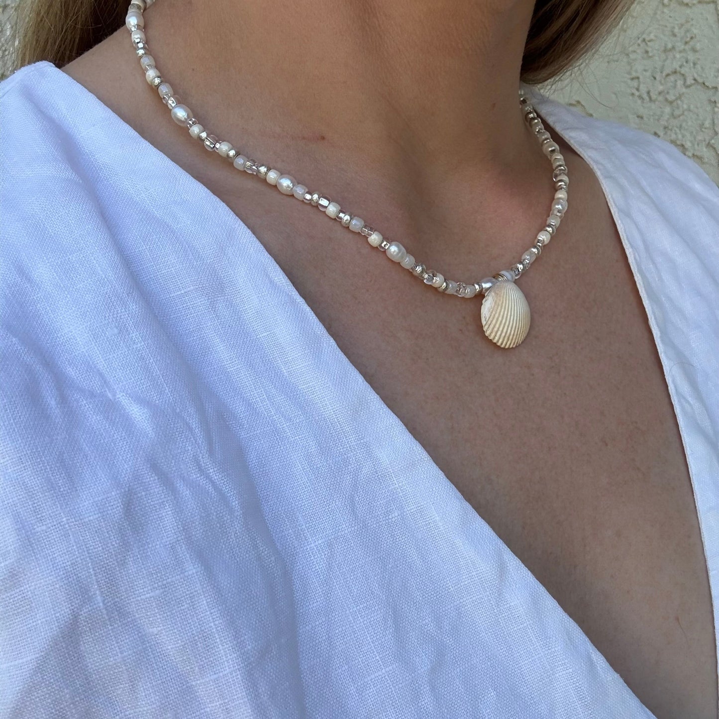 Pearl necklace with a shell pendant worn by a person in a white top.