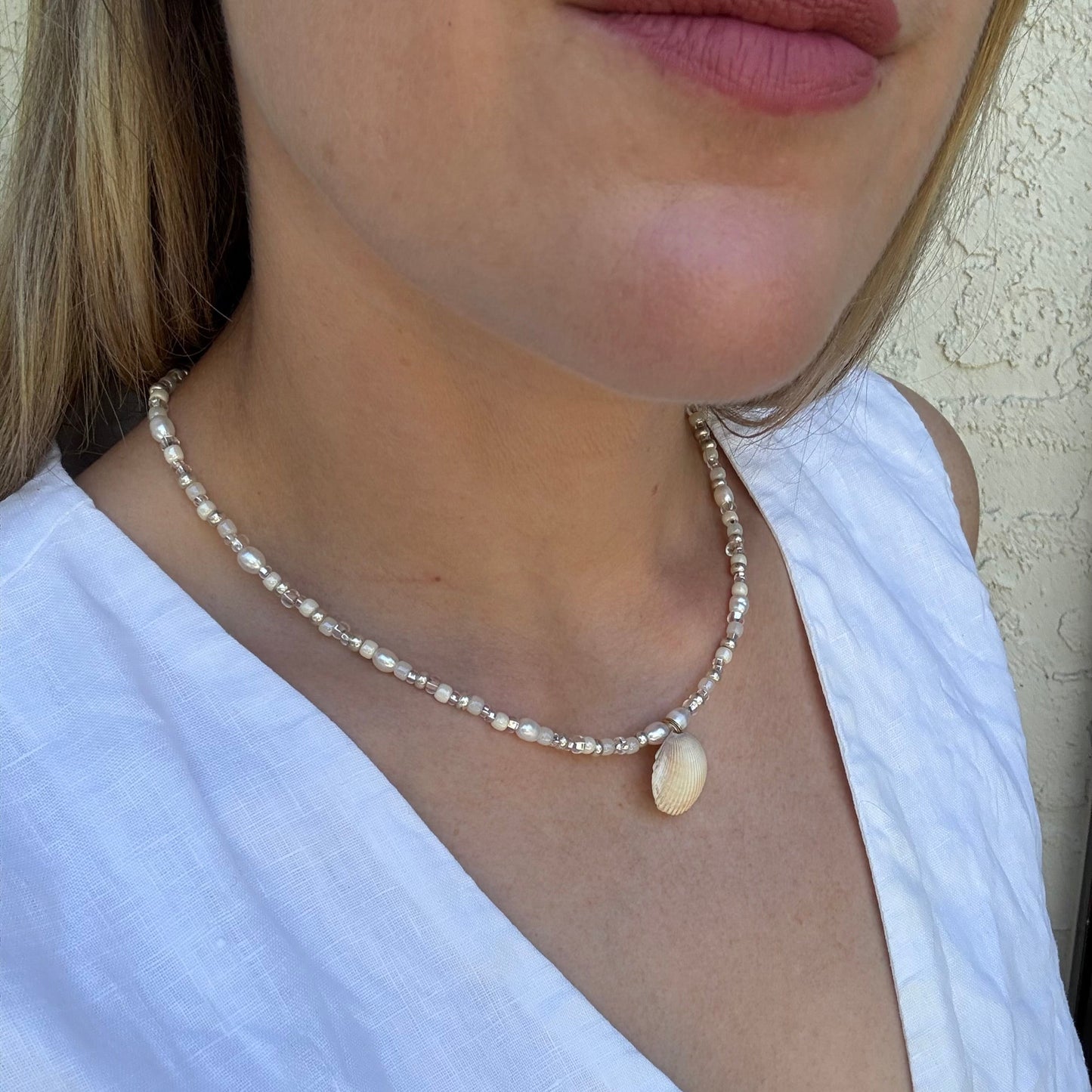 Pearl necklace with a large central bead worn by a person in a white top.