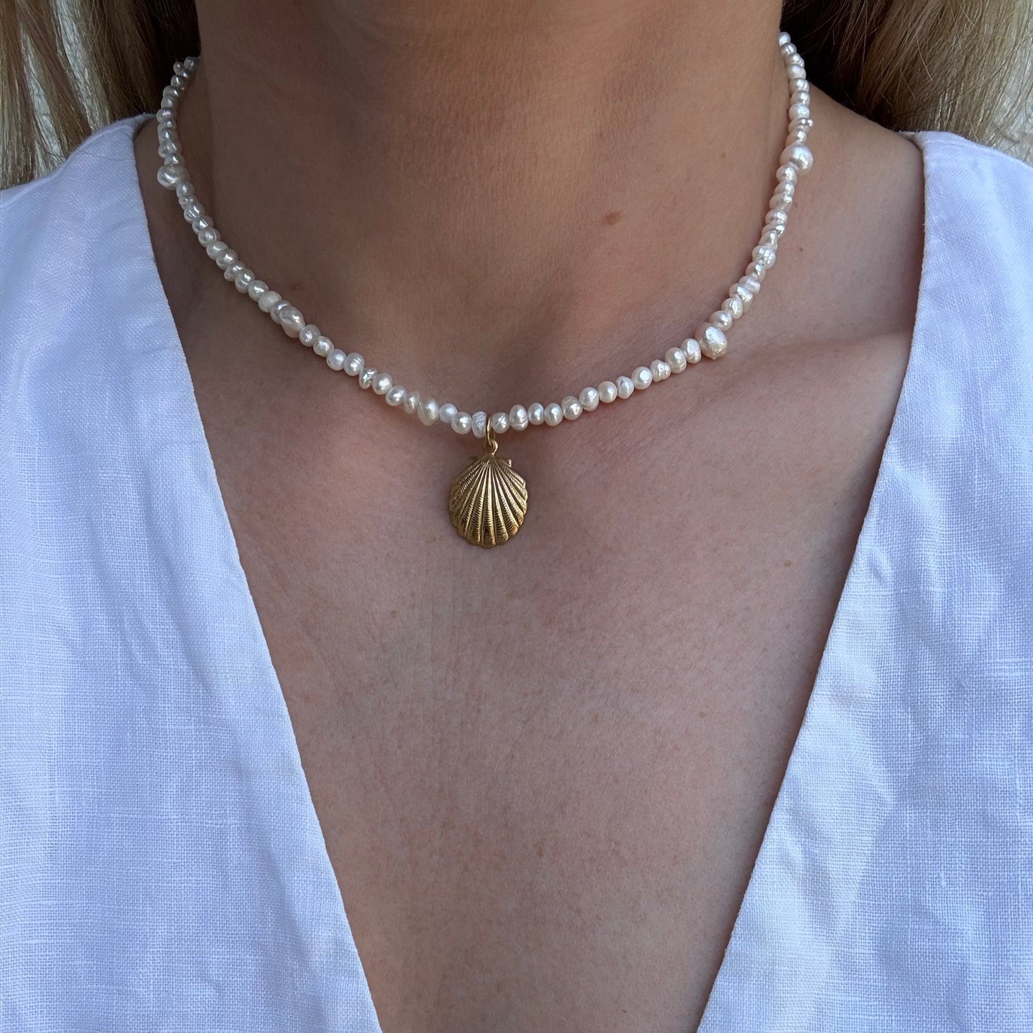 Pearl necklace with a gold shell pendant worn by a person in a white top.