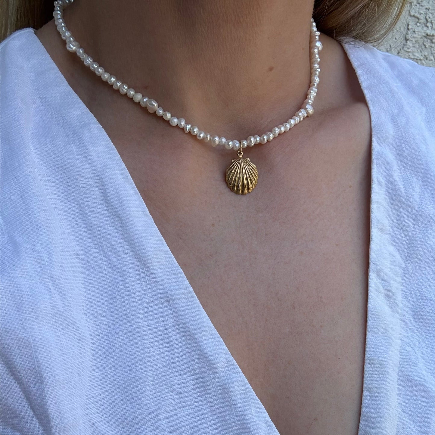 Pearl necklace with a gold shell pendant on a white blouse