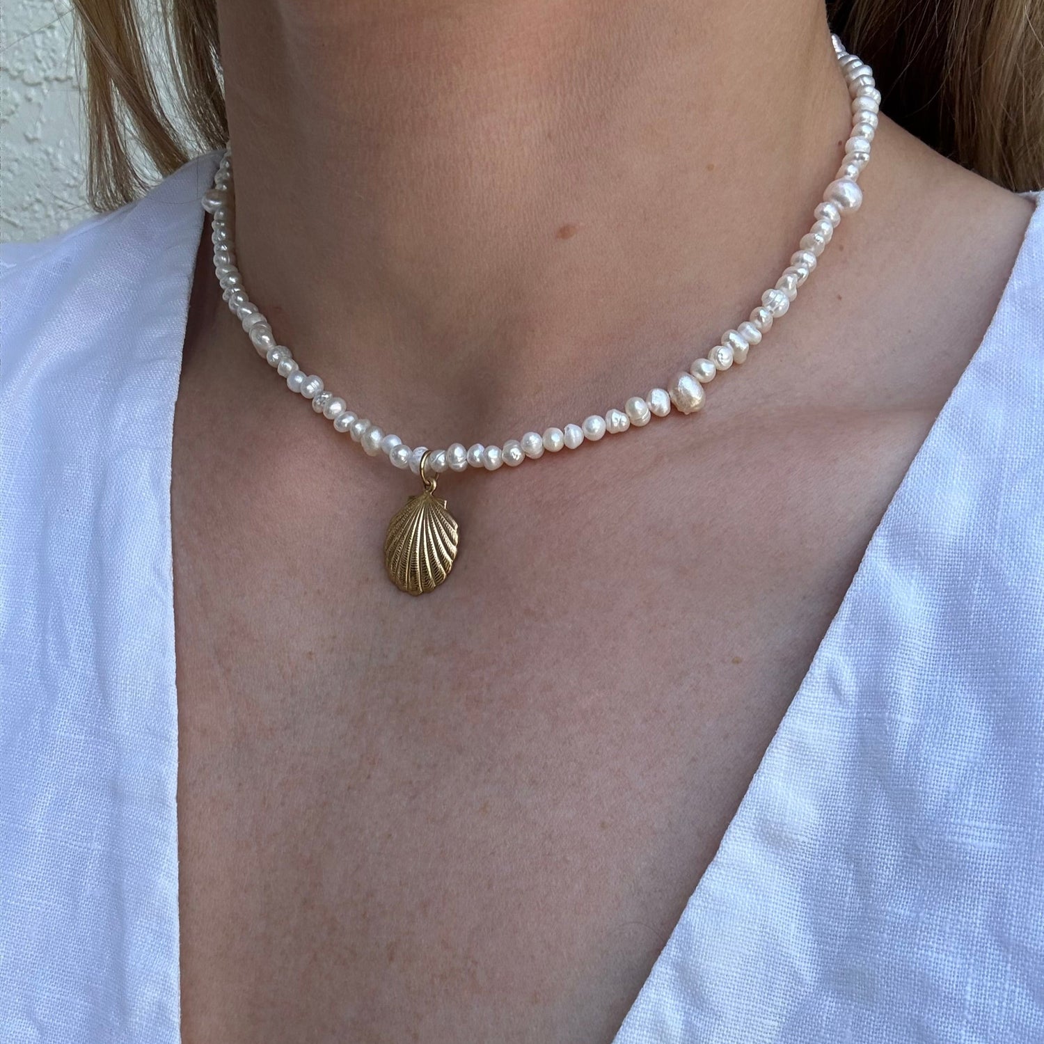 Pearl necklace with a gold shell pendant worn by a person in a white shirt.