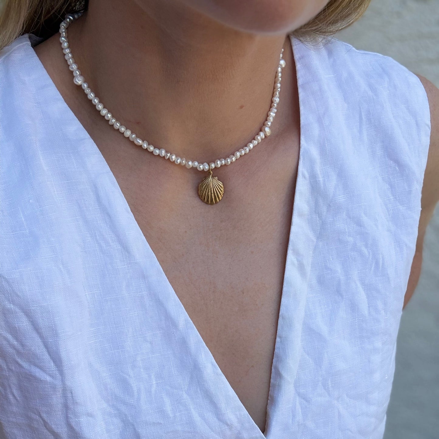 Pearl necklace with a gold clasp worn by a person in a white sleeveless top.