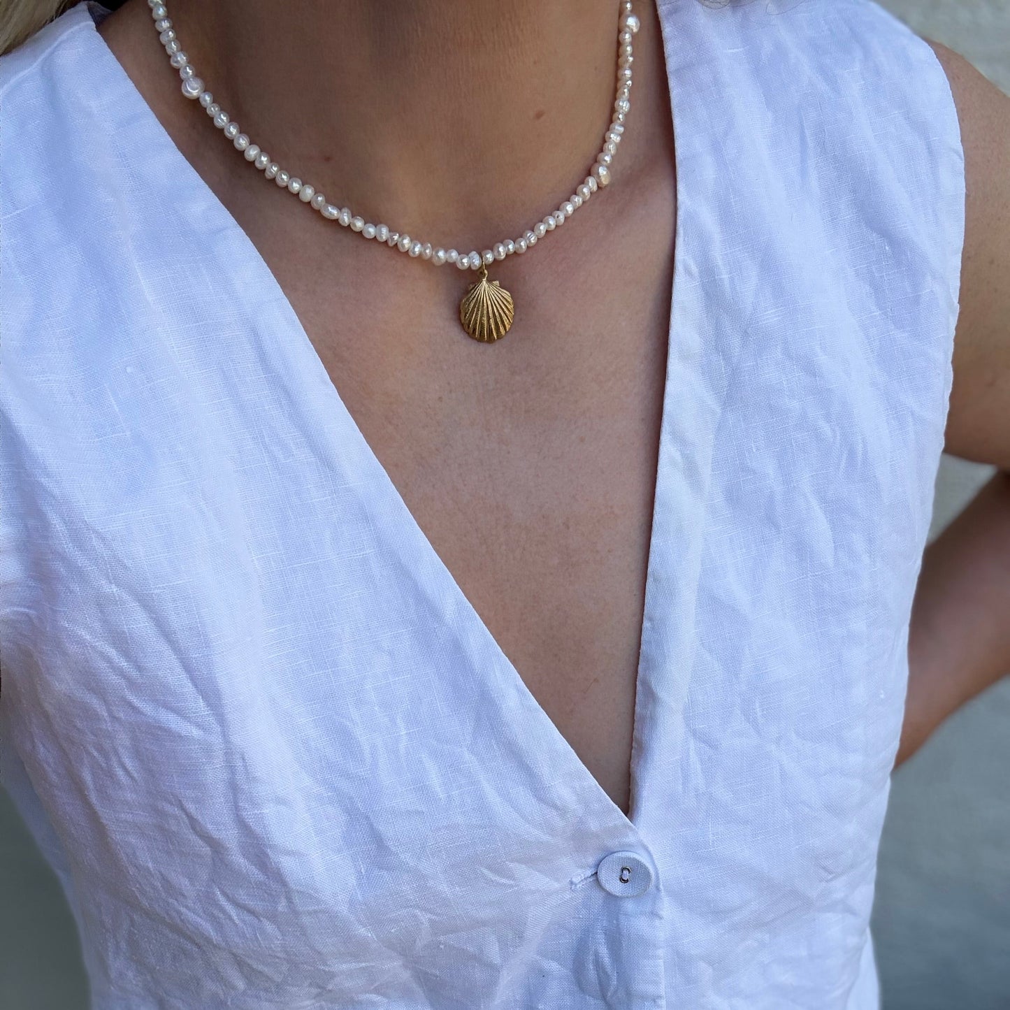 Person wearing a white sleeveless top and a pearl necklace with a shell pendant.