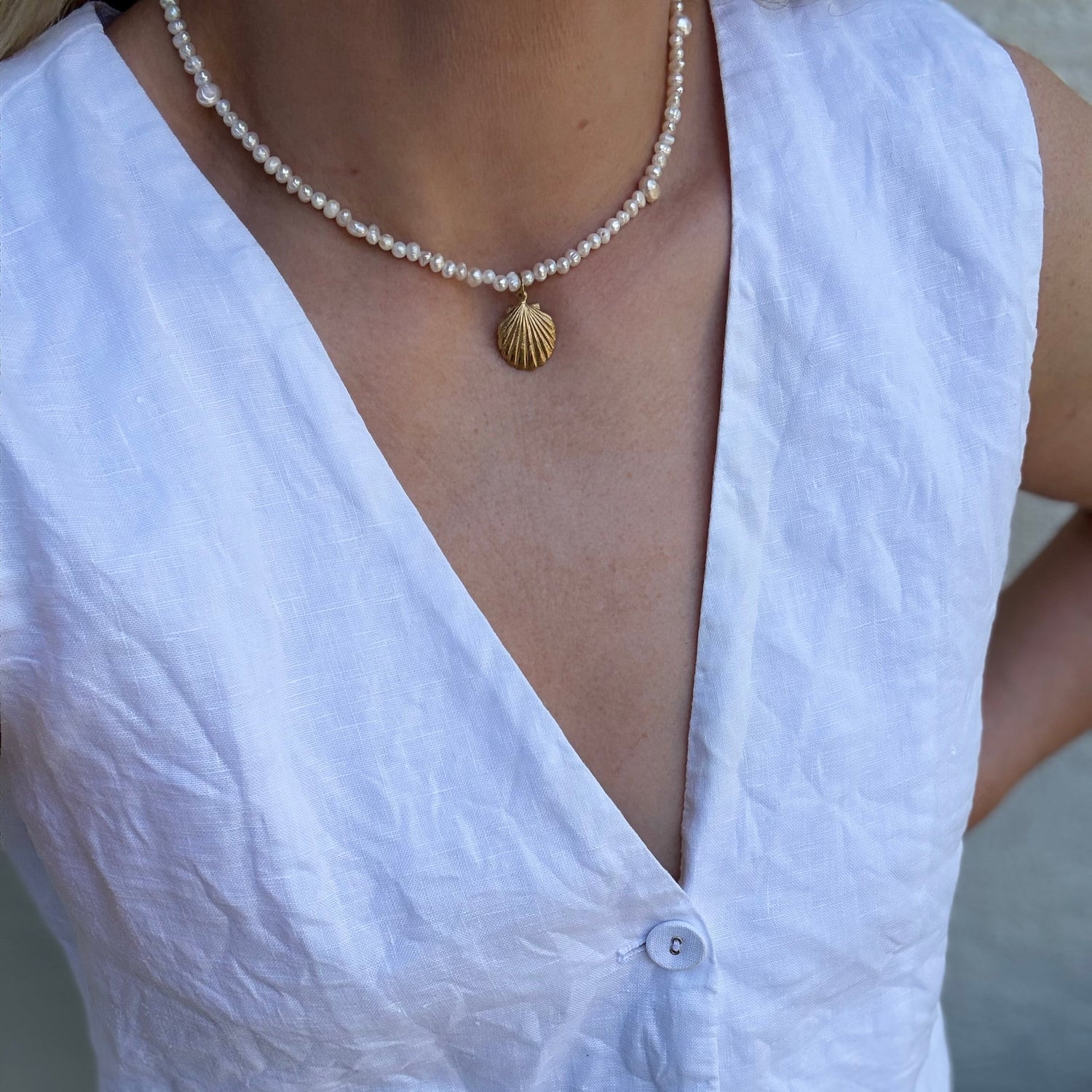 Person wearing a white sleeveless top and a pearl necklace with a shell pendant.