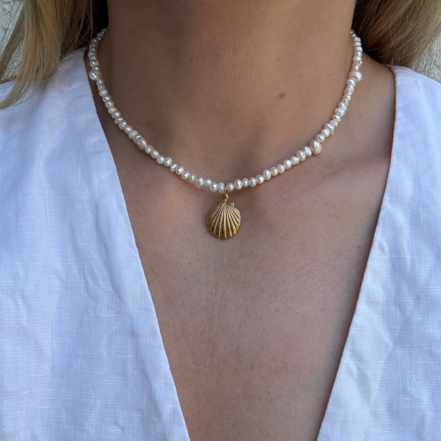 Pearl necklace with a gold shell pendant on a white shirt