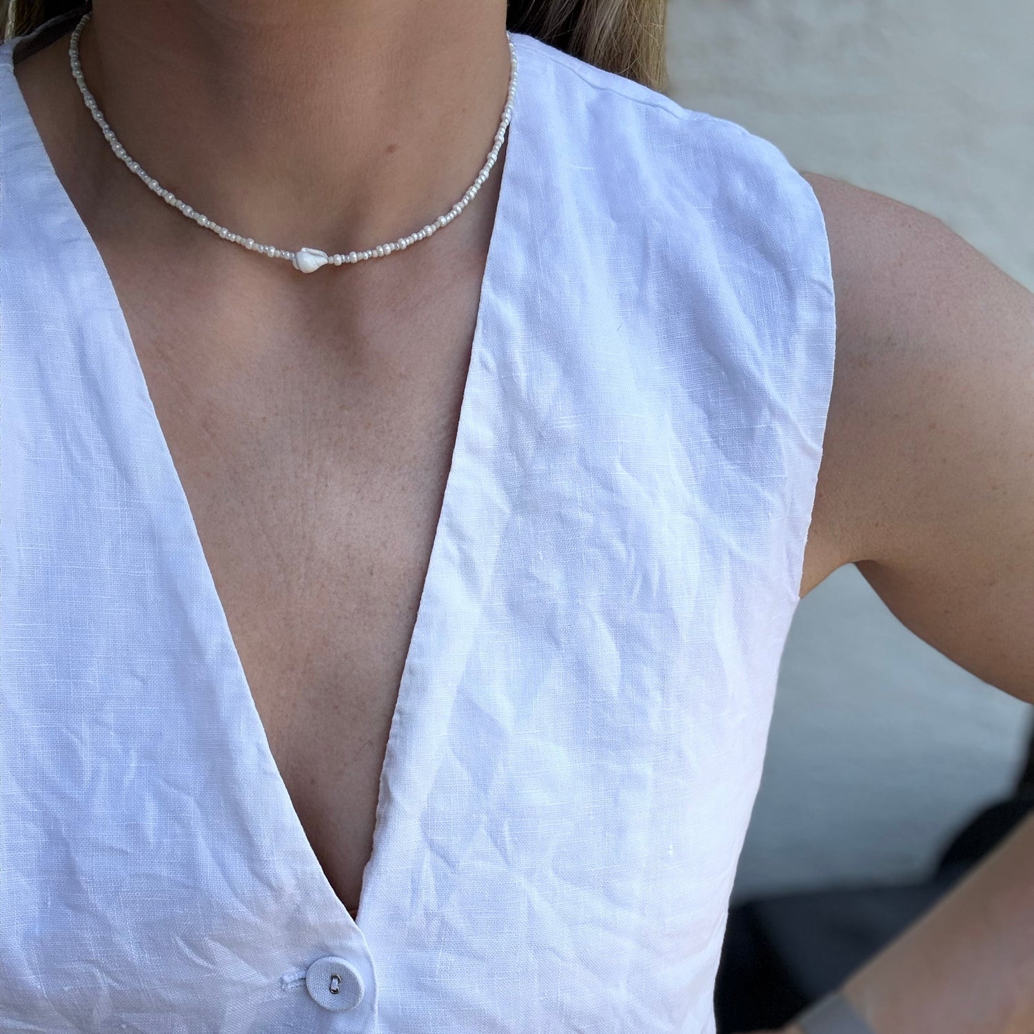 White sleeveless top worn by a person, with a pearl necklace and bracelet.