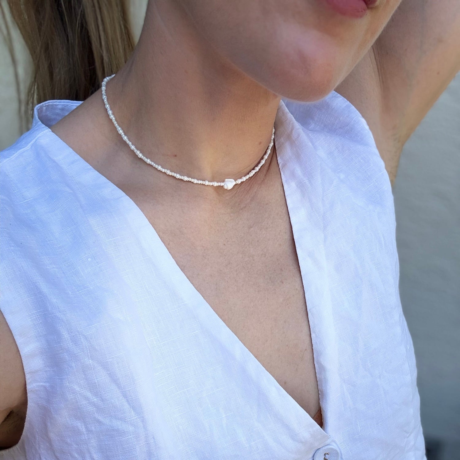 Person wearing a delicate necklace with a white top.