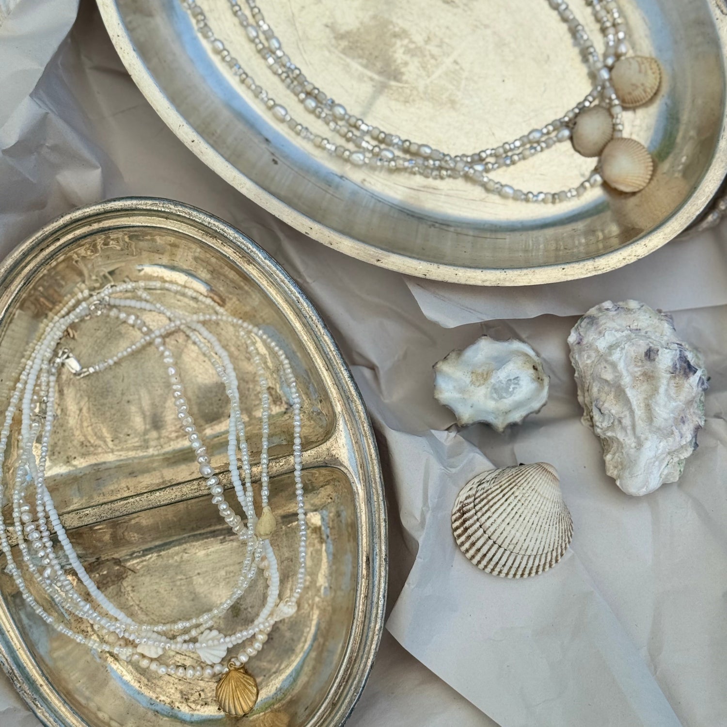 Silver jewelry box with layered necklaces and seashells on a white surface