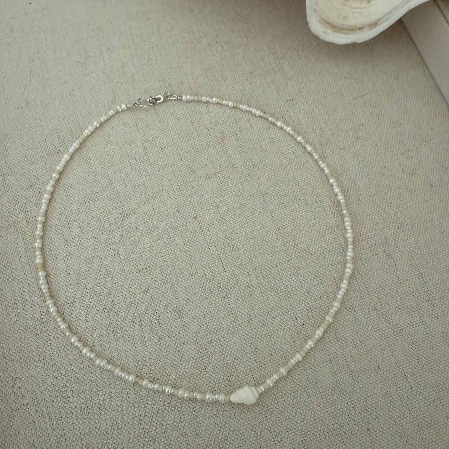 Pearl necklace on a textured surface with a shell