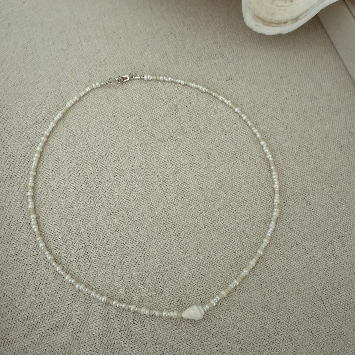 Pearl necklace on a textured surface with a shell