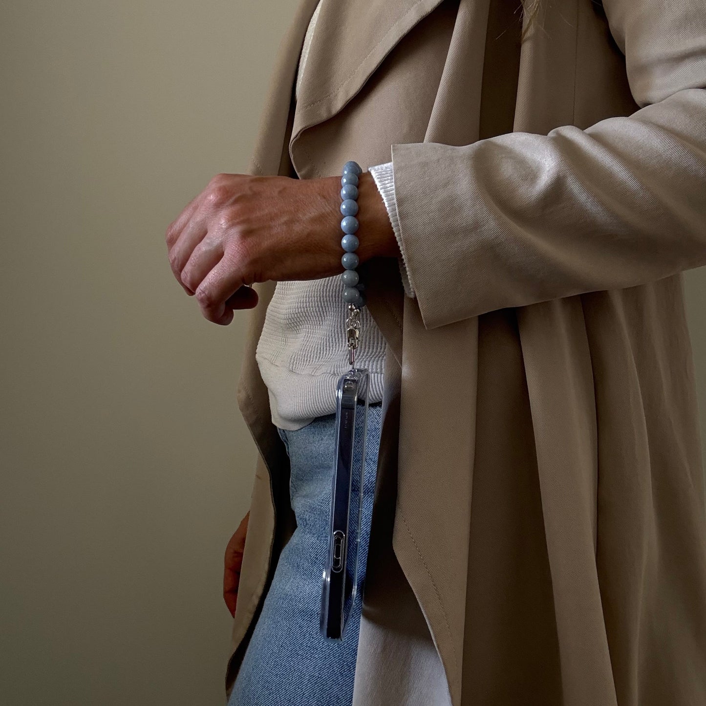 Person wearing a beige trench coat with blue beaded mobile phone chain