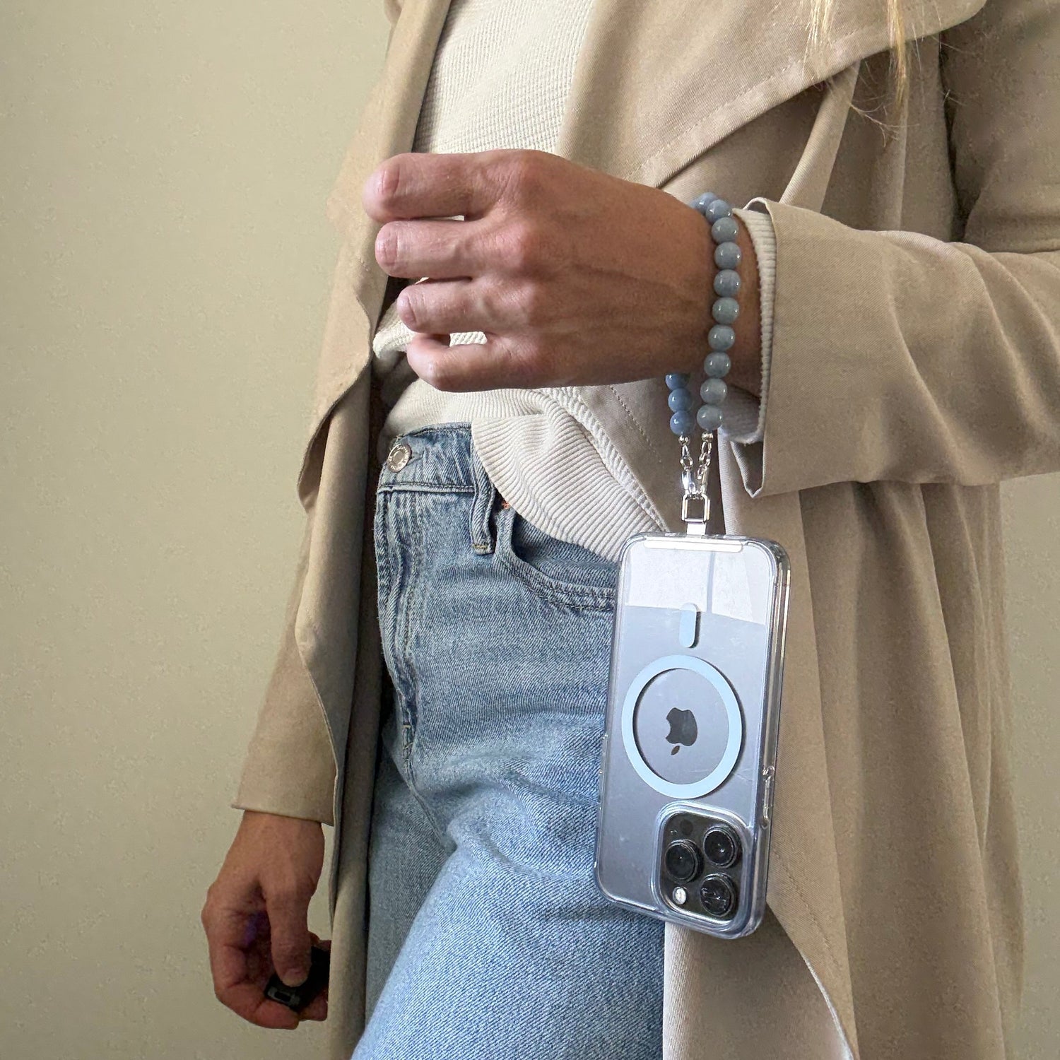 Person wearing a beige trench coat with a blue beaded mobile phone chain.