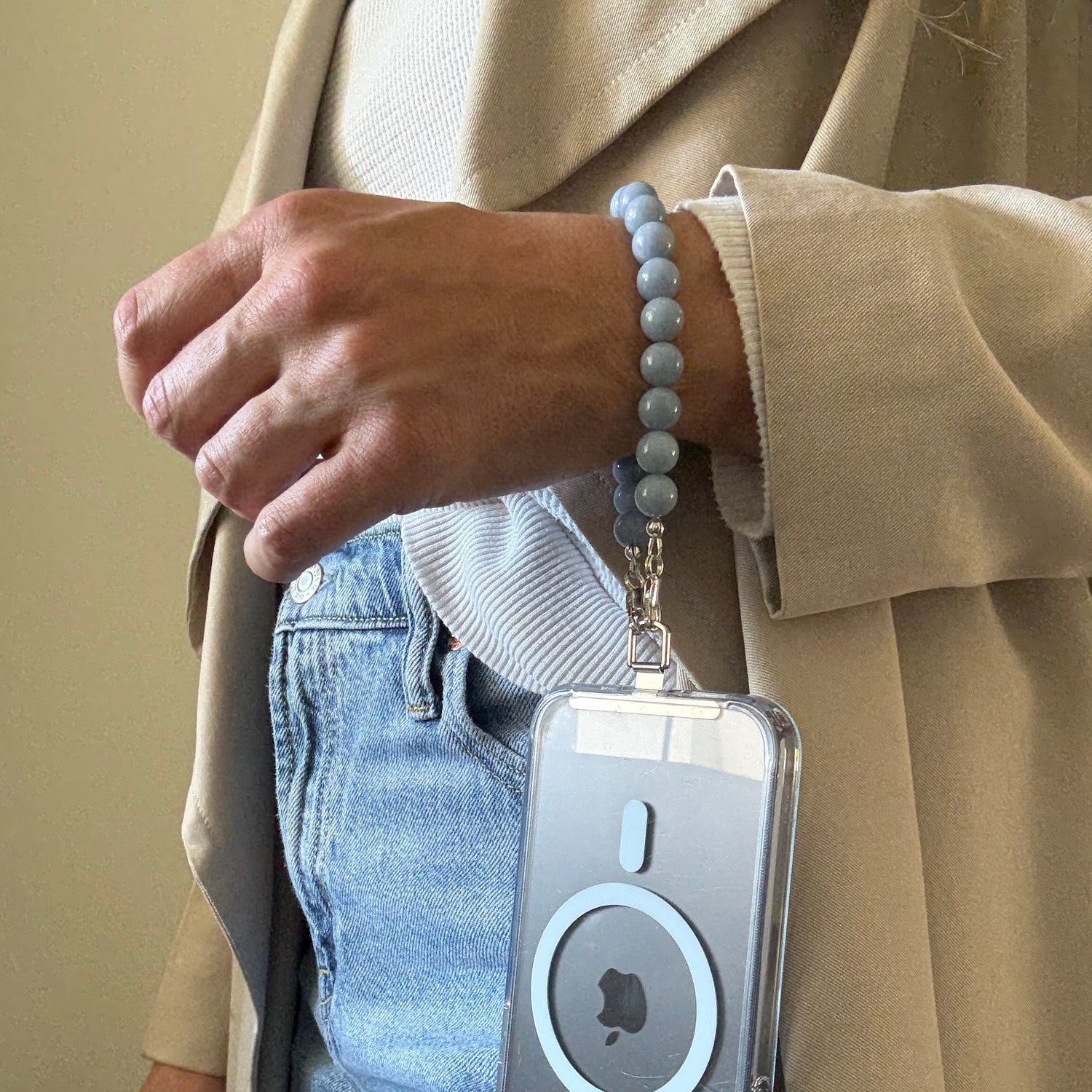 Person holding a mobile phone chain, wearing a beige jacket and blue jeans.