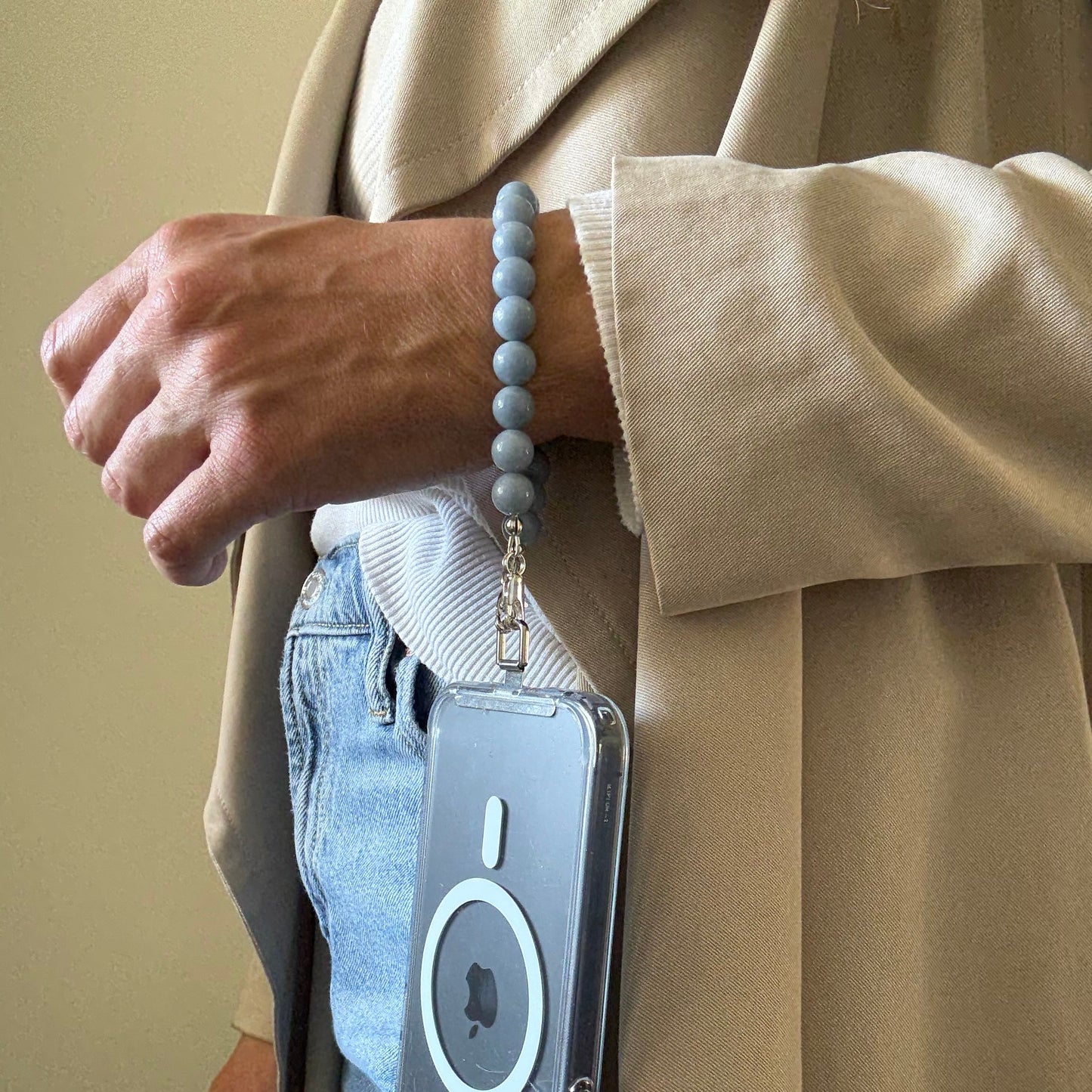 Person holding a  blue beaded mobile phone chain with a visible brand logo against a neutral background